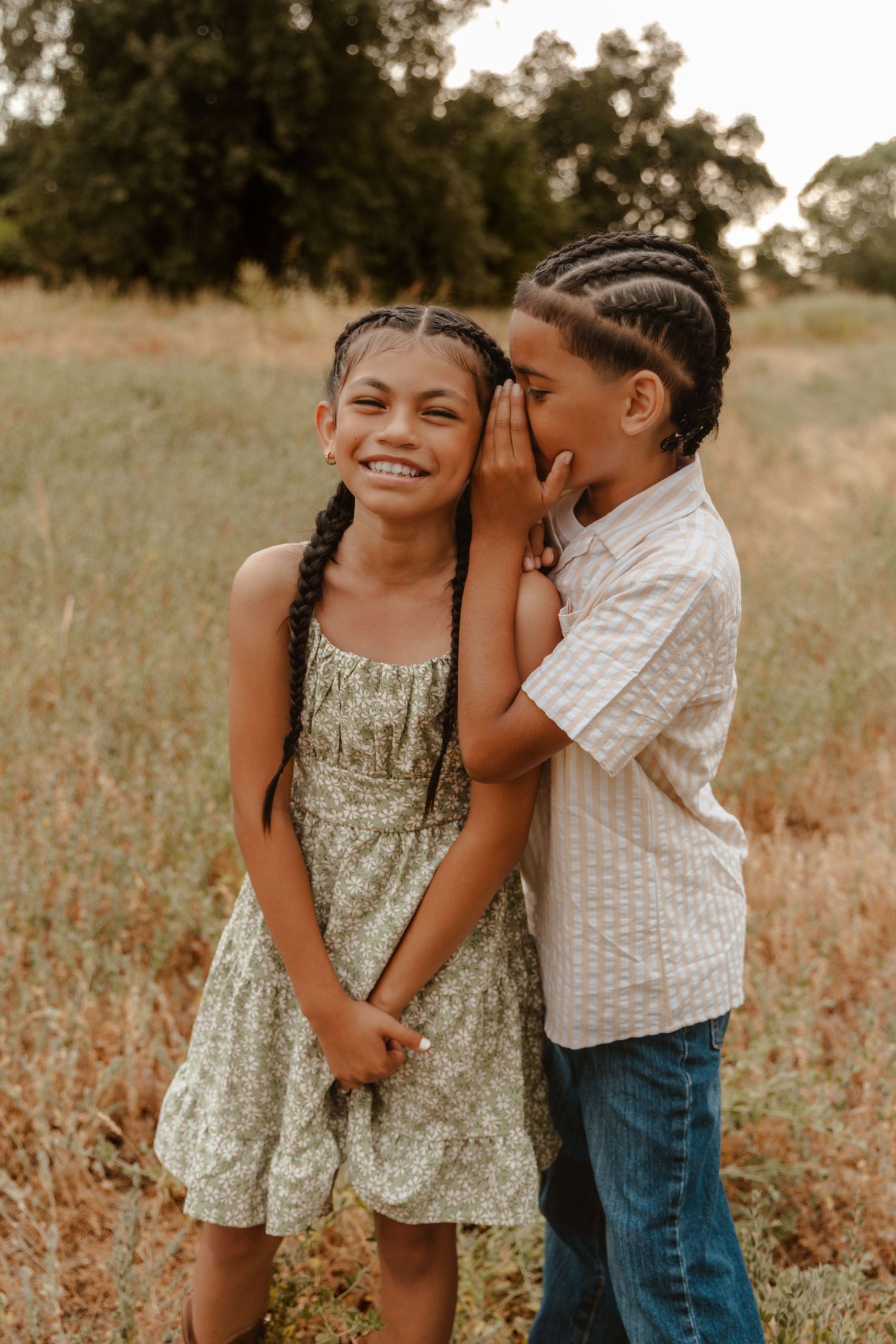Two children playing and sharing secrets in a golden field during sunset.