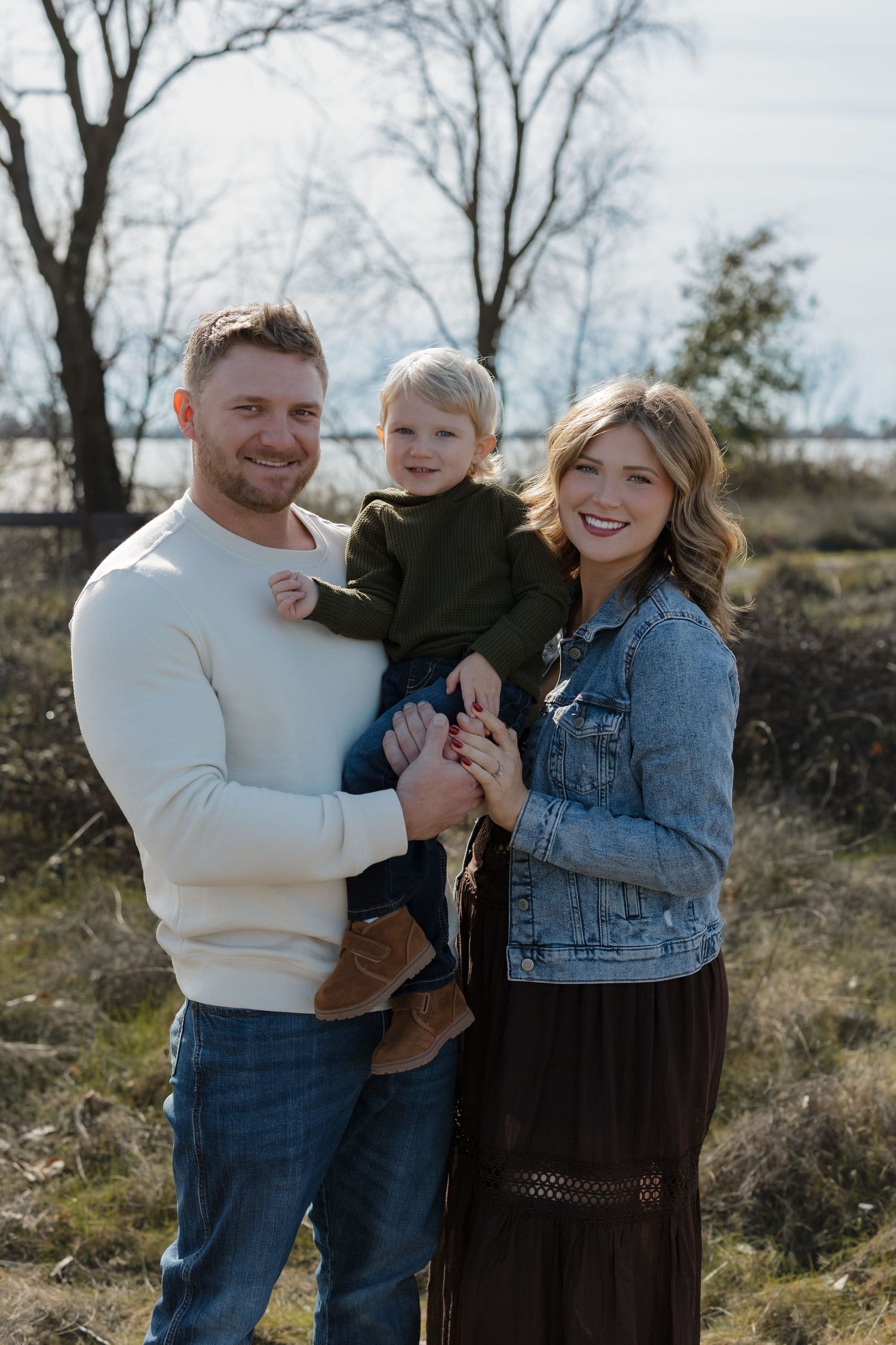 A family poses together outdoors on a winter day in casual attire against a natural backdrop.