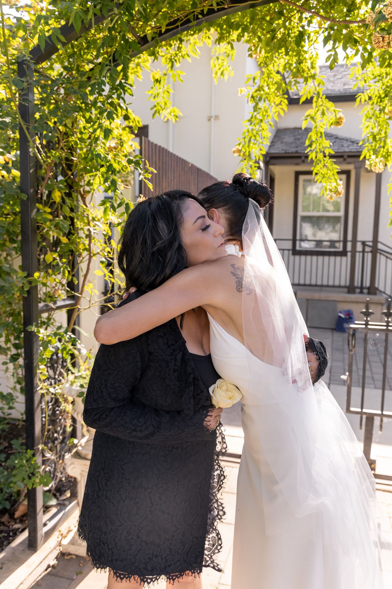 Wedding couple embraces in a sunny garden setting with white dress and black attire.