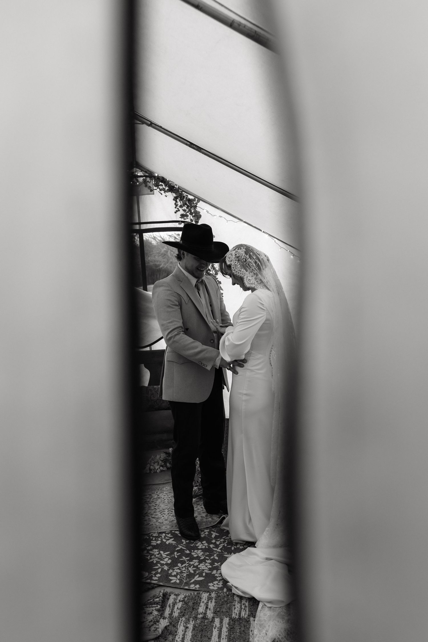 A black and white artistic wedding photo captured through a doorway or window frame.