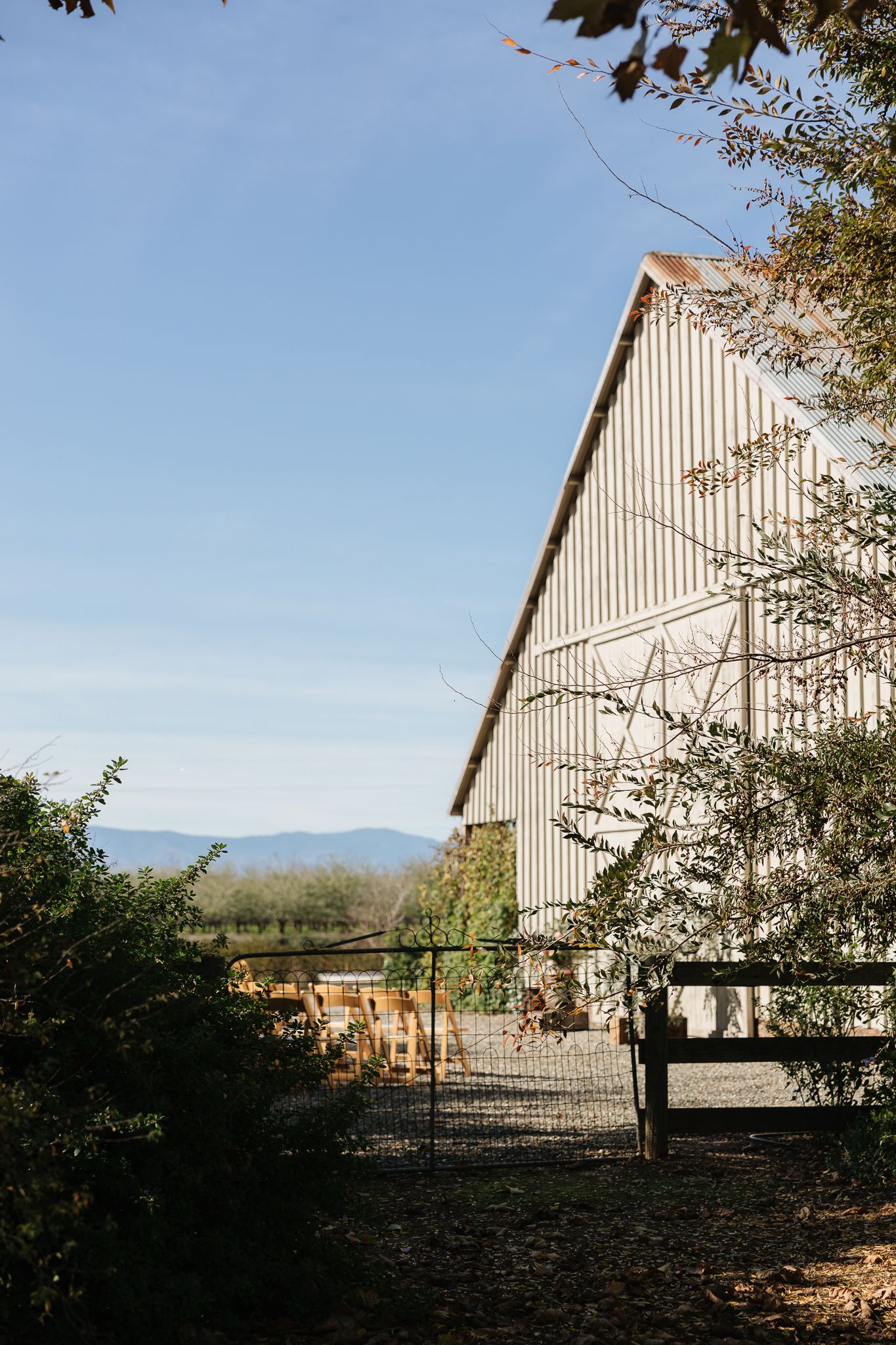 A large white barn structure with mountain views in the background on a clear day.