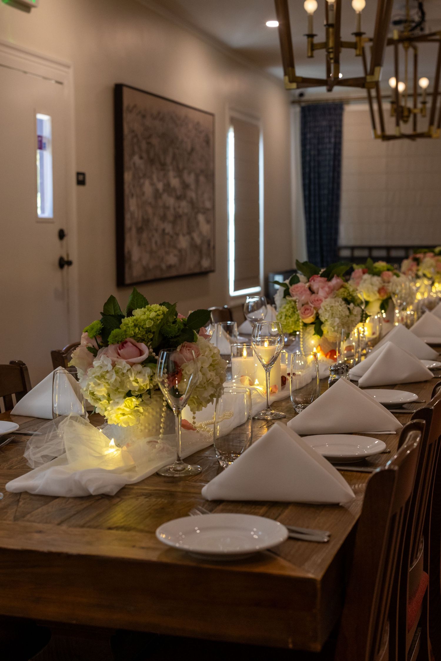Elegant wedding reception table setting with glowing candles and white napkins in a rustic dining room.