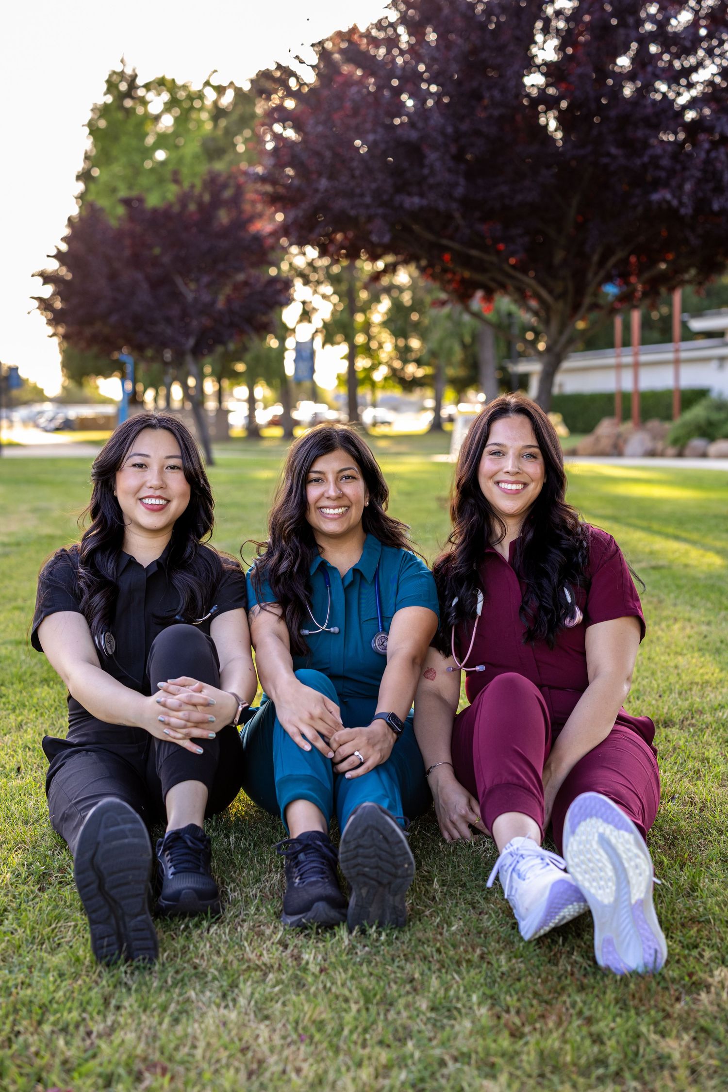Group nursing graduates sit on campus lawn in scrubs for nursing graduate photos by Your Moments by Kelli