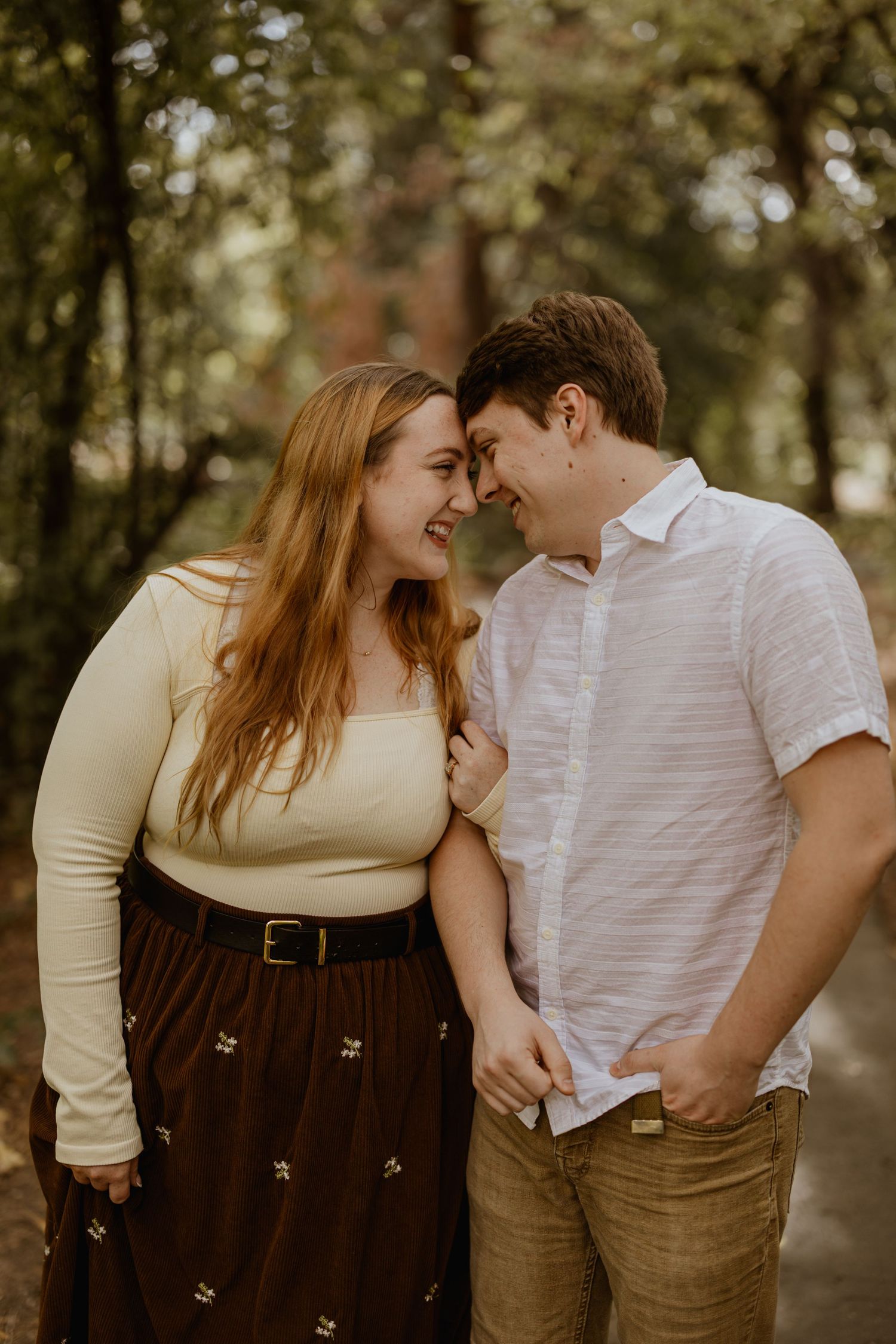 Couple sharing intimate moment in wooded area during autumn photoshoot.