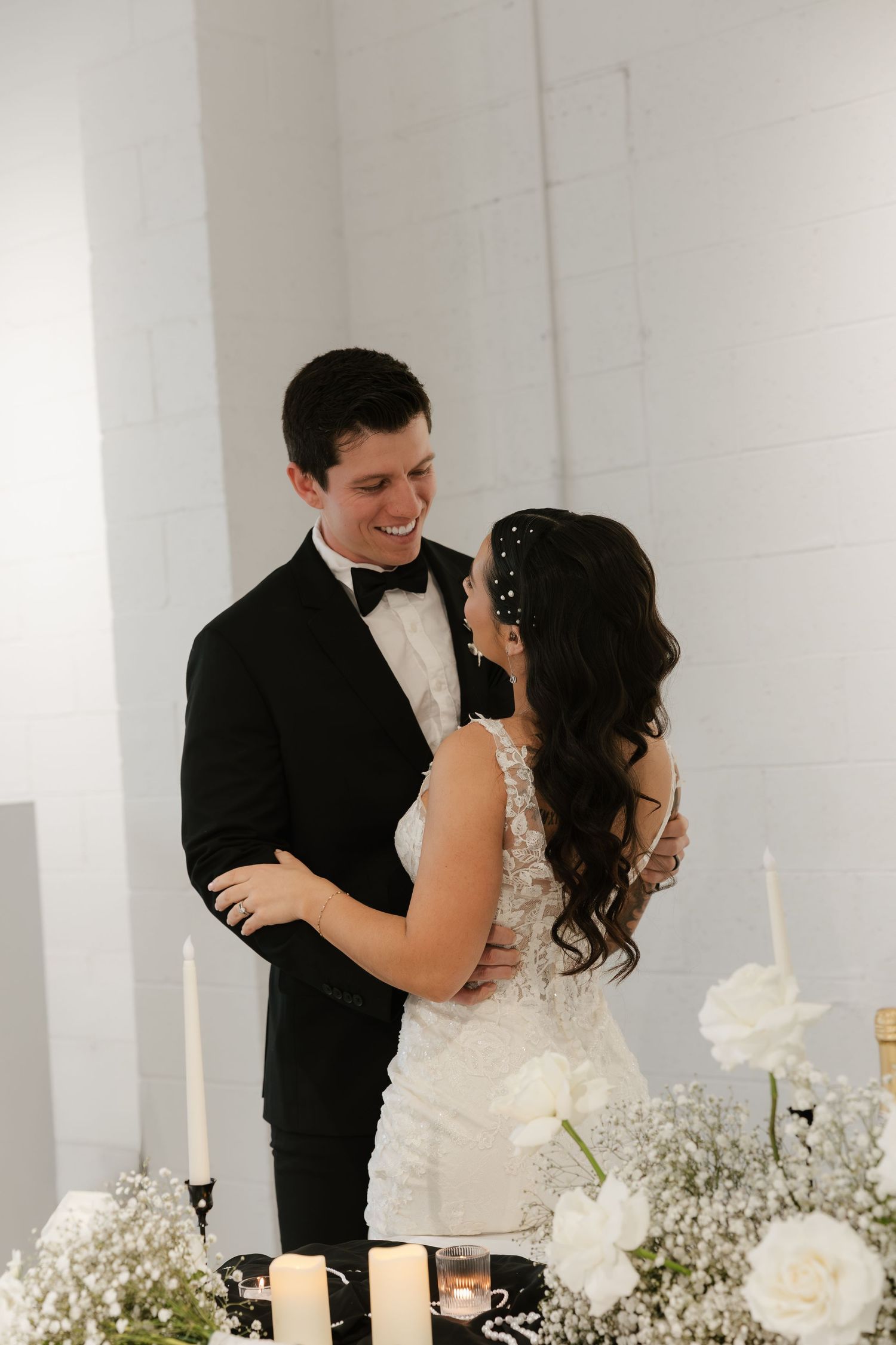 A romantic moment between newlyweds sharing laughter at their wedding reception with white roses and decor.
