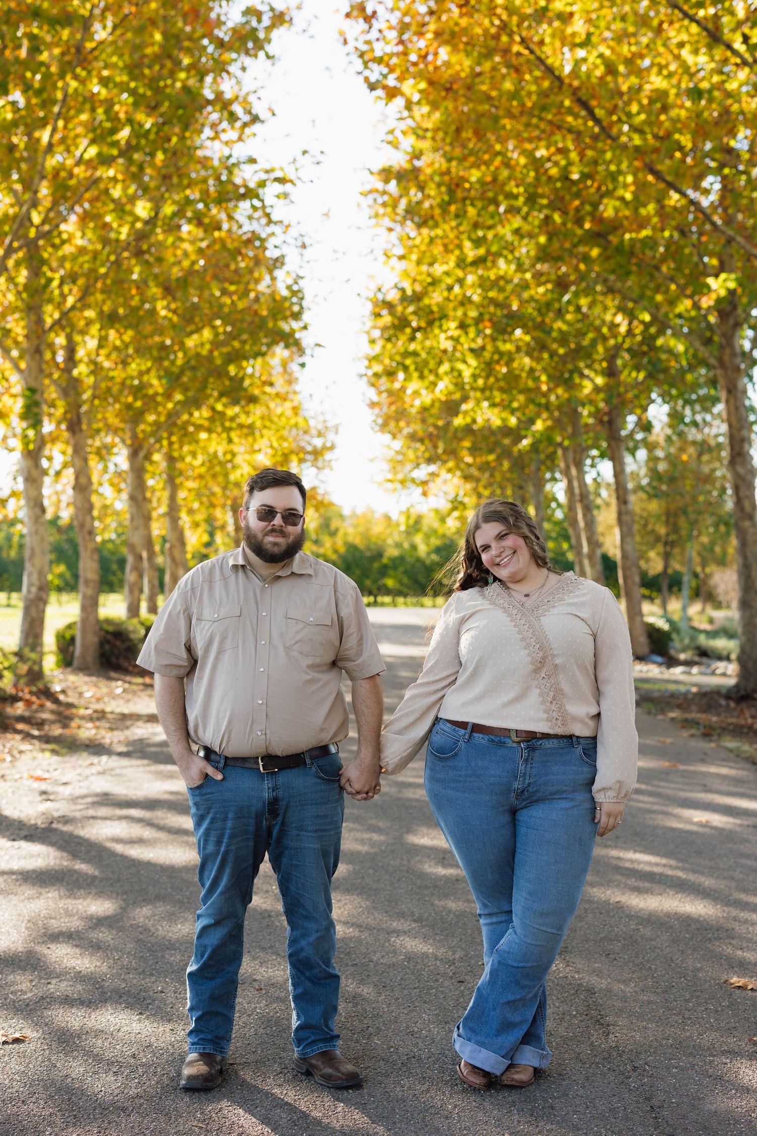 Couple holding hands while walking on path lined with golden autumn trees.