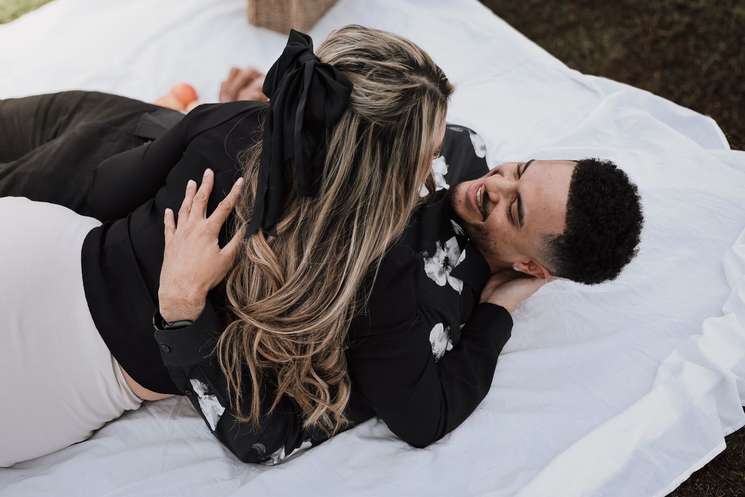 A couple lying in the snow wearing winter coats share a romantic moment together.