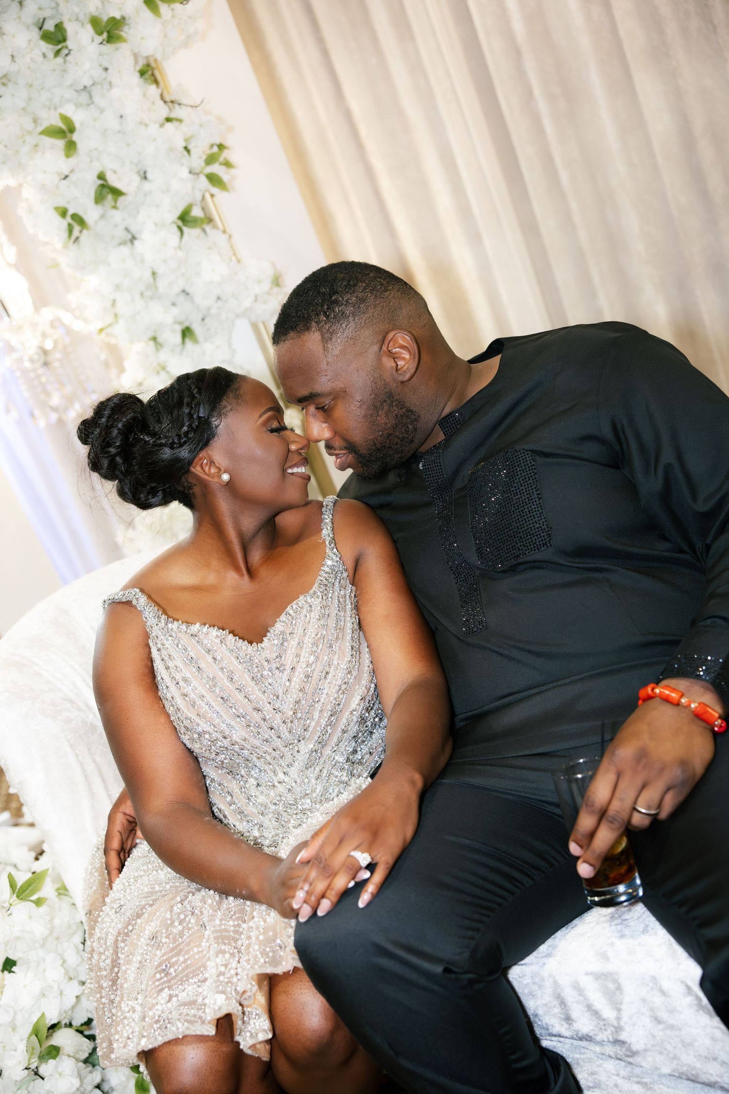 Couple in elegant attire sharing a romantic moment at a wedding reception with white floral backdrop.