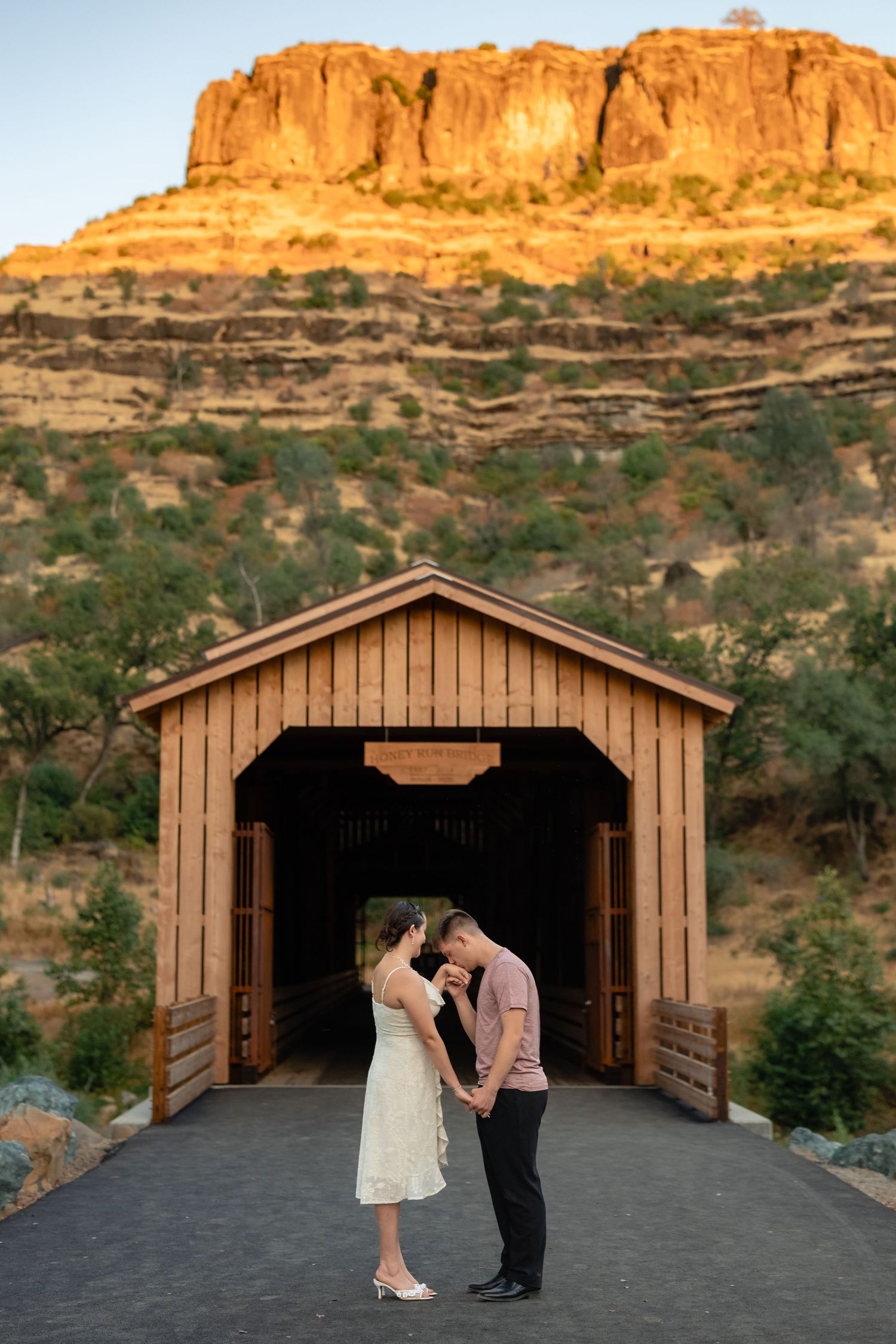 A couple shares a romantic moment in front of a wooden structure with red rock cliffs behind them.