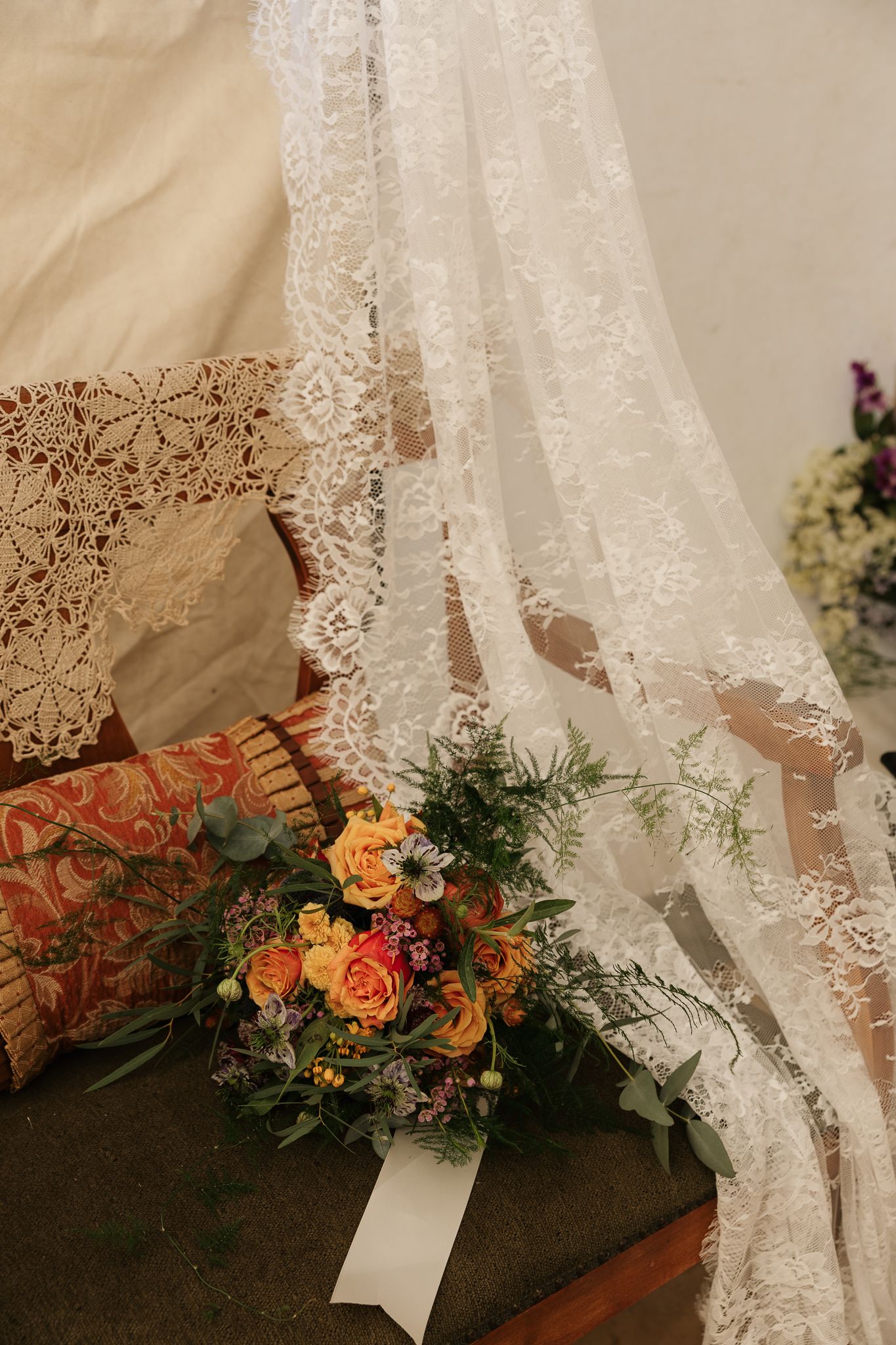 A delicate white lace veil drapes near a bouquet of peach roses and greenery against a cushioned background.