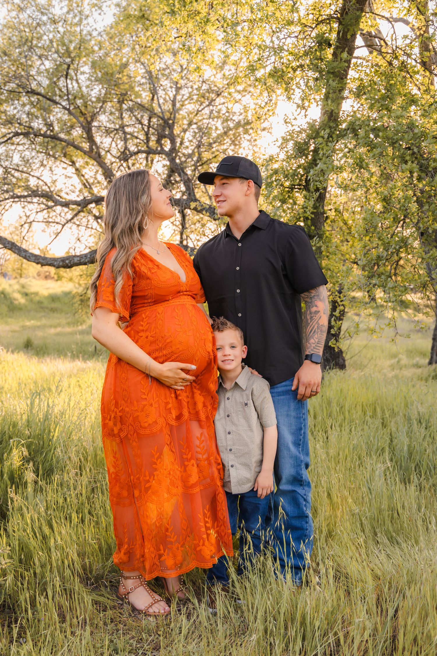 A family portrait session in tall grass with golden sunlight filtering through trees.