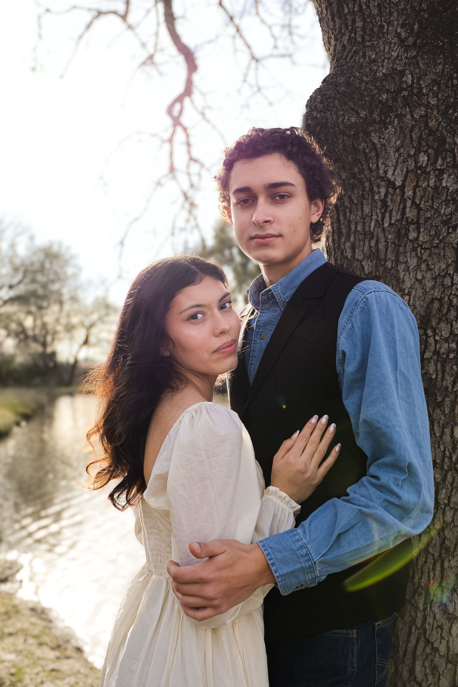Romantic couple's portrait session against tree trunk with soft natural lighting.