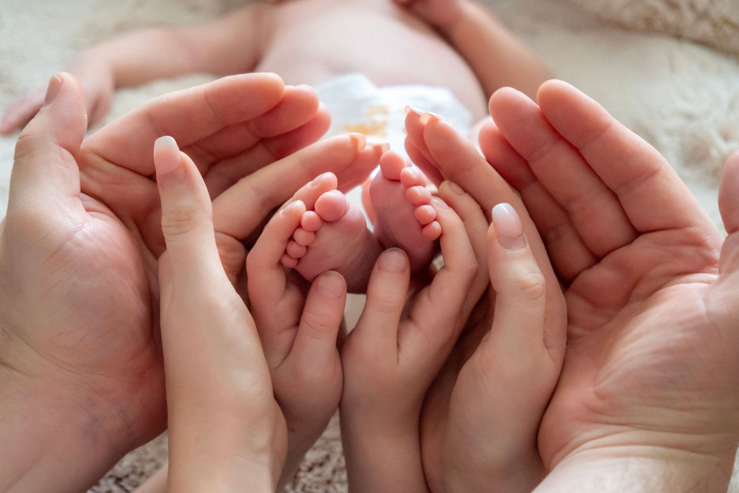 Adult hands cradling tiny newborn baby feet, symbolizing love and family protection.