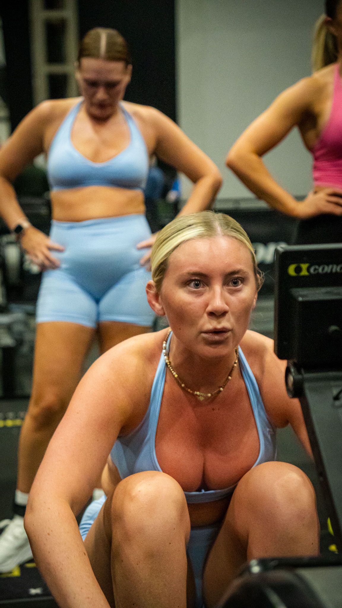 Women in blue athletic wear working out in a gym, focusing on fitness training with rowing equipment.
