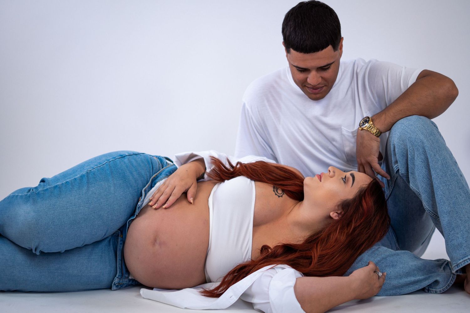 A man tenderly looks at his pregnant partner as she reclines during a maternity photoshoot.