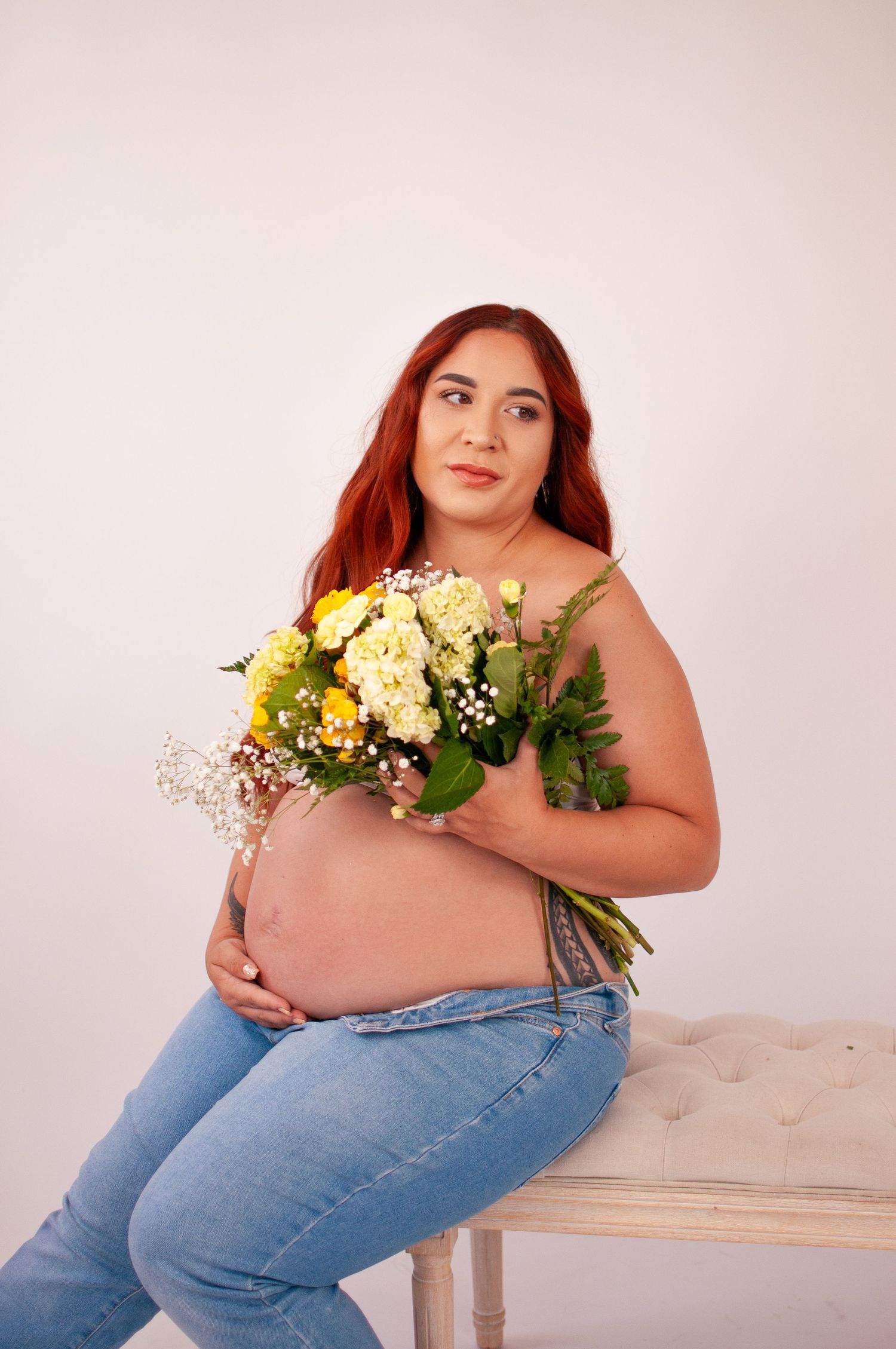 Pregnant redhead woman holding yellow and white flower bouquet in studio portrait.
