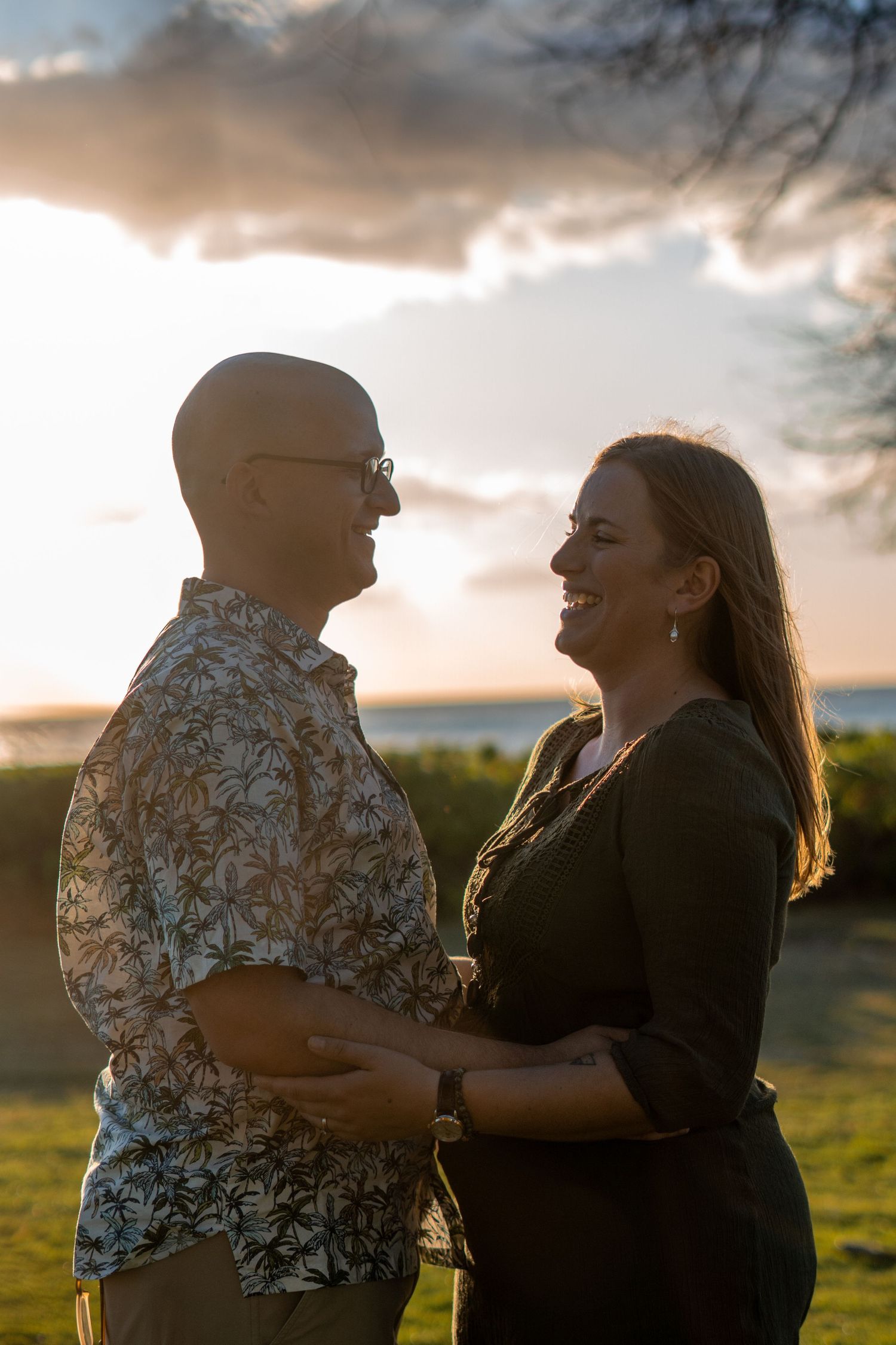 Smiling couple embraces outdoors during warm golden sunset near the ocean.