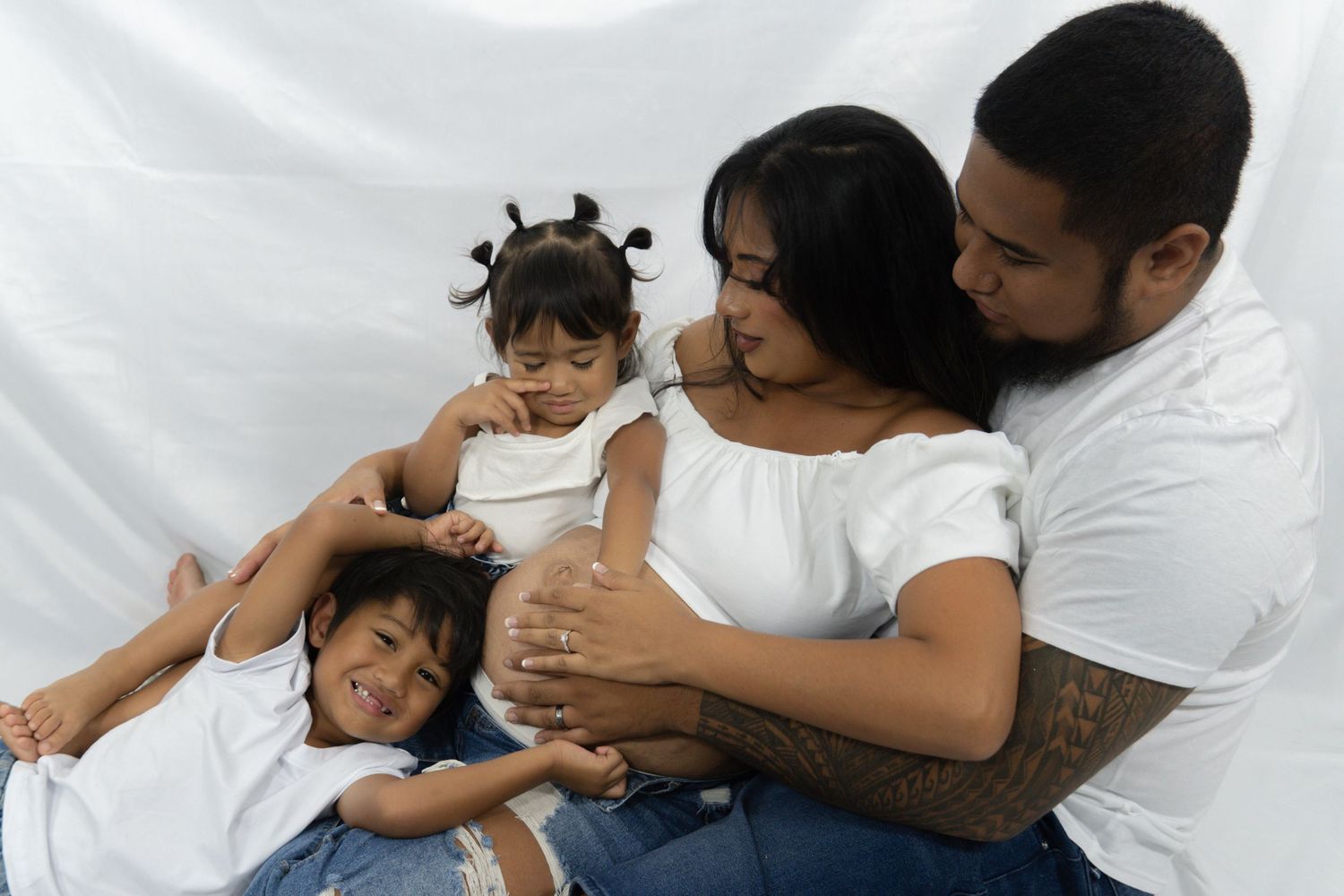 Happy Latino family with two young daughters poses together on white backdrop.