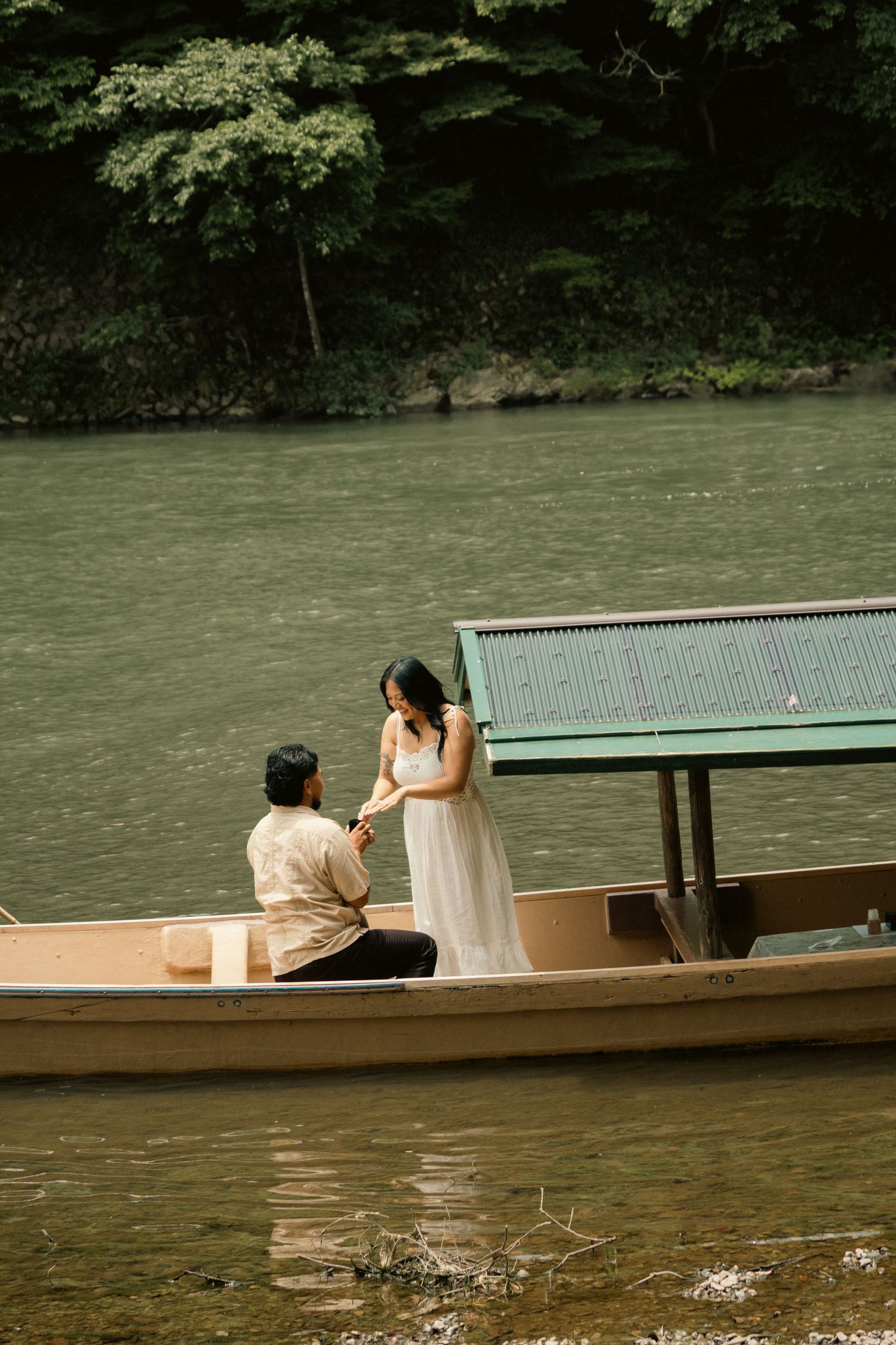Couple in wedding attire sharing a romantic moment on a wooden boat on a serene river.