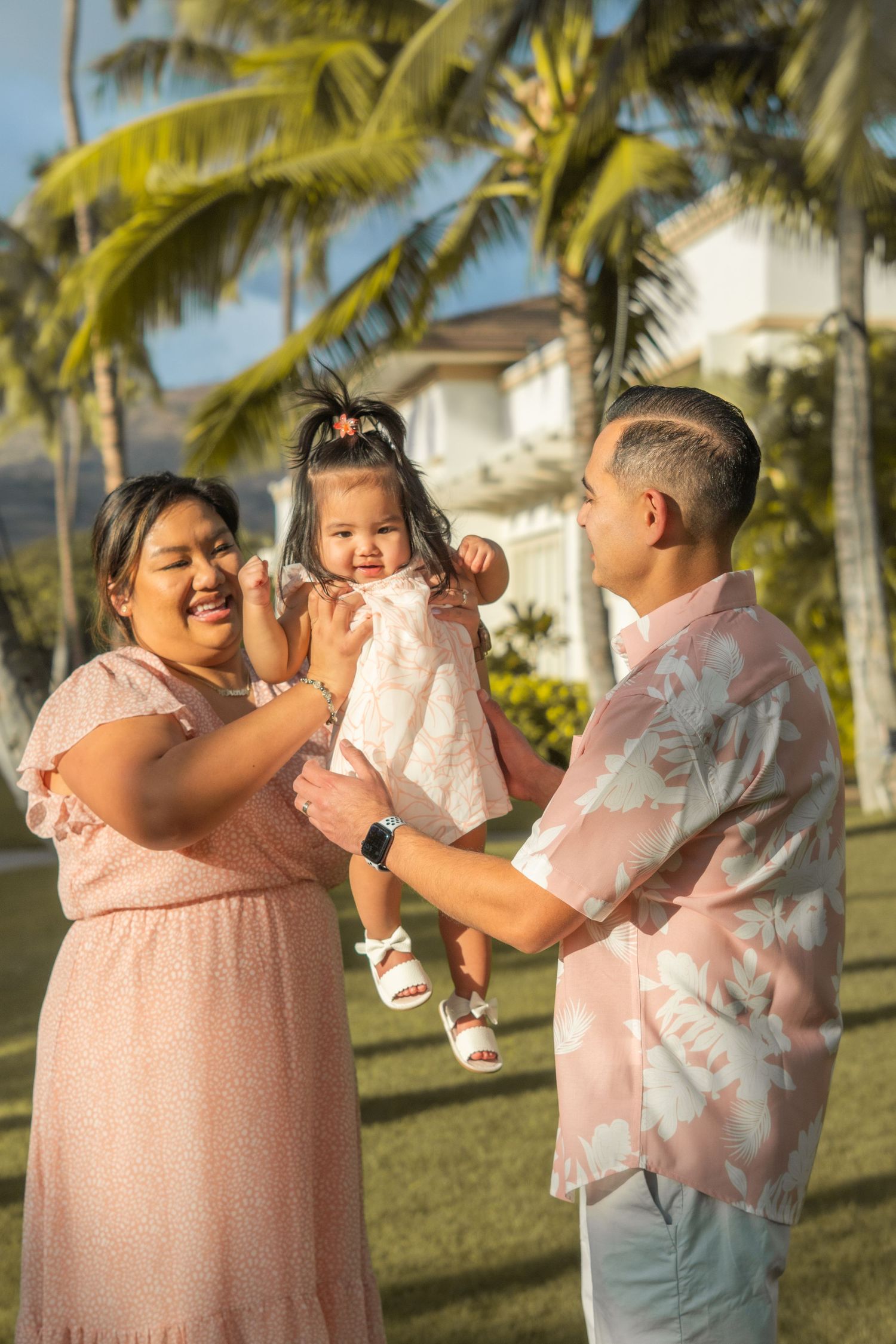 Happy family with parents and baby daughter playing under palm trees in Hawaii.