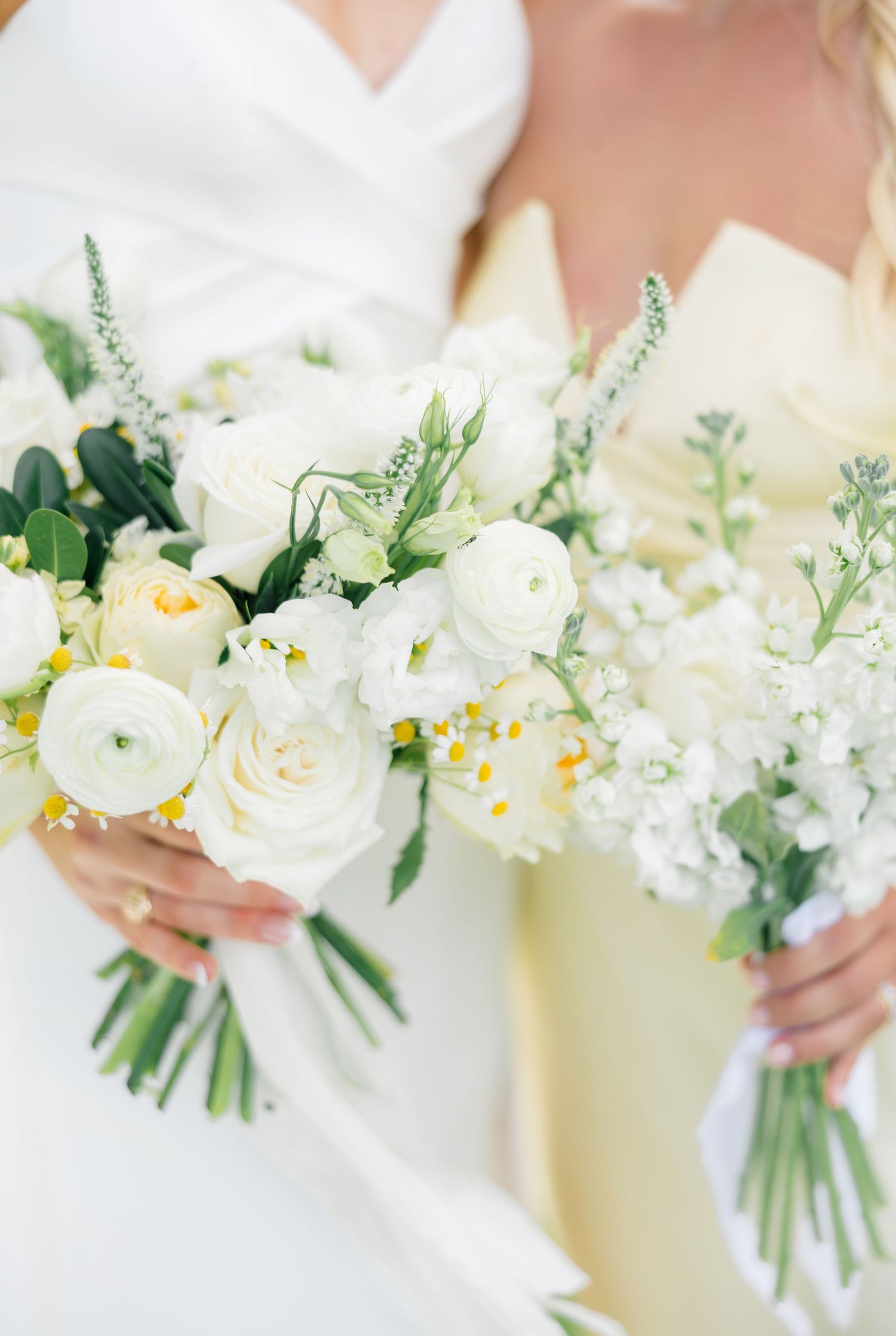 A delicate wedding bouquet featuring ranunculus, roses, and greenery held against a light background at Chandelier Farms Terrell TX.