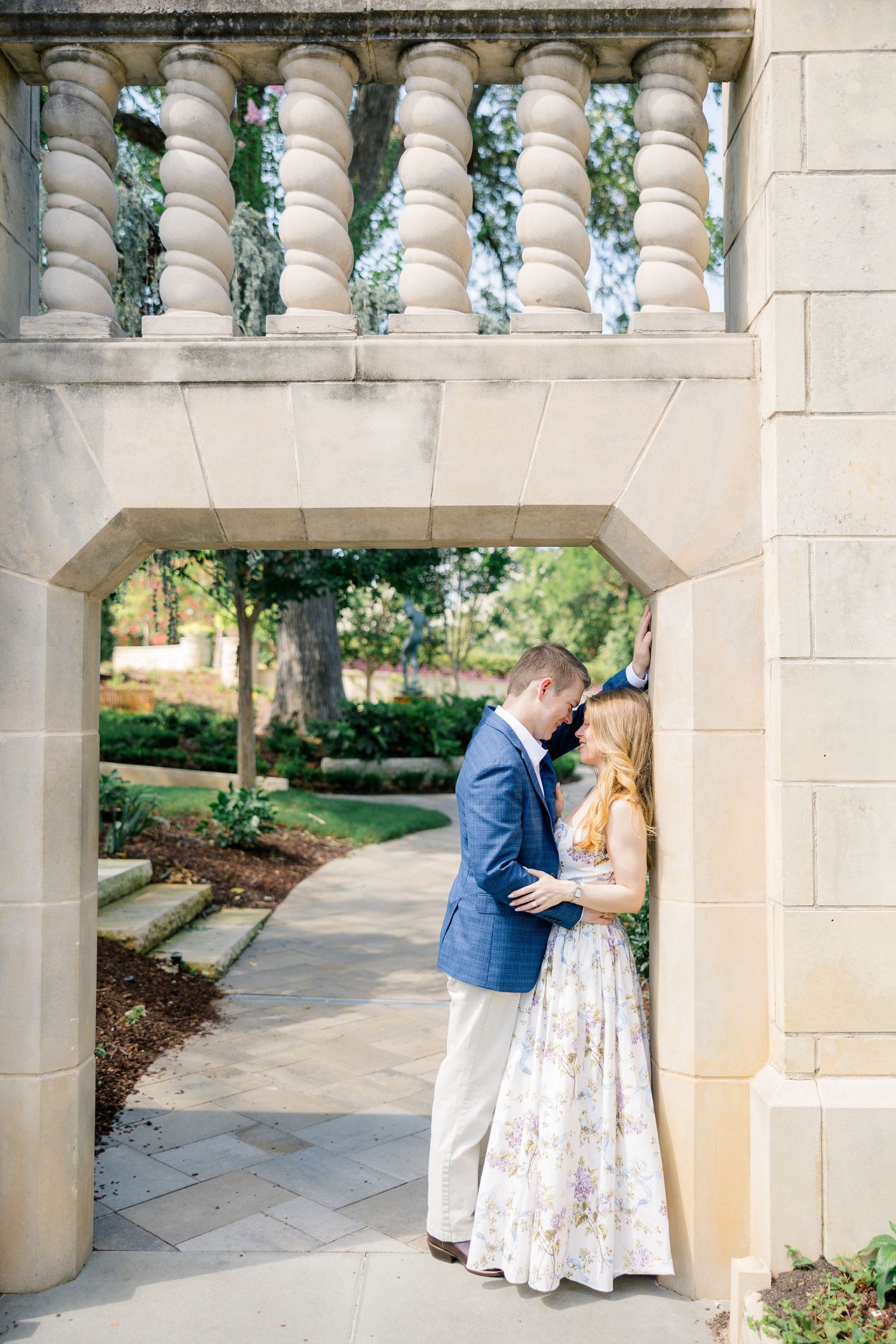 Couple shares a romantic moment under a stone arch in a garden, in the Women's Garden Dallas Arboretum