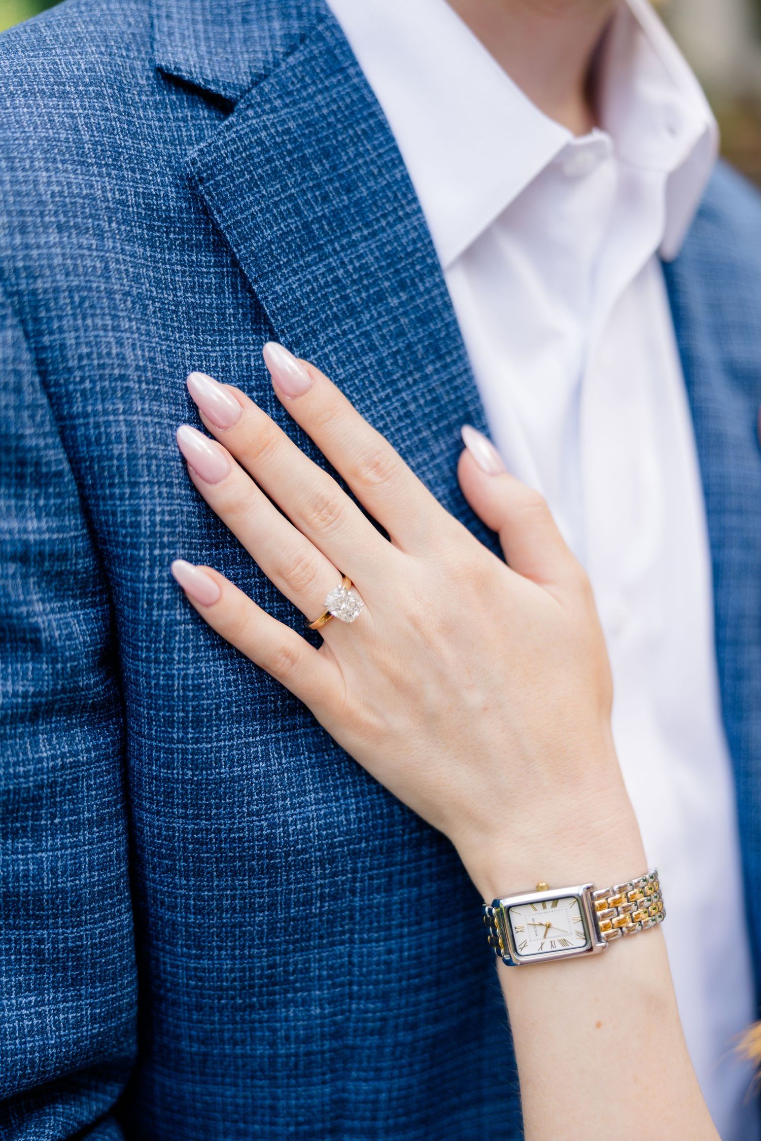 Woman's hand with diamond engagement ring and gold watch resting on man's blue tweed suit jacket at Dallas Arboretum