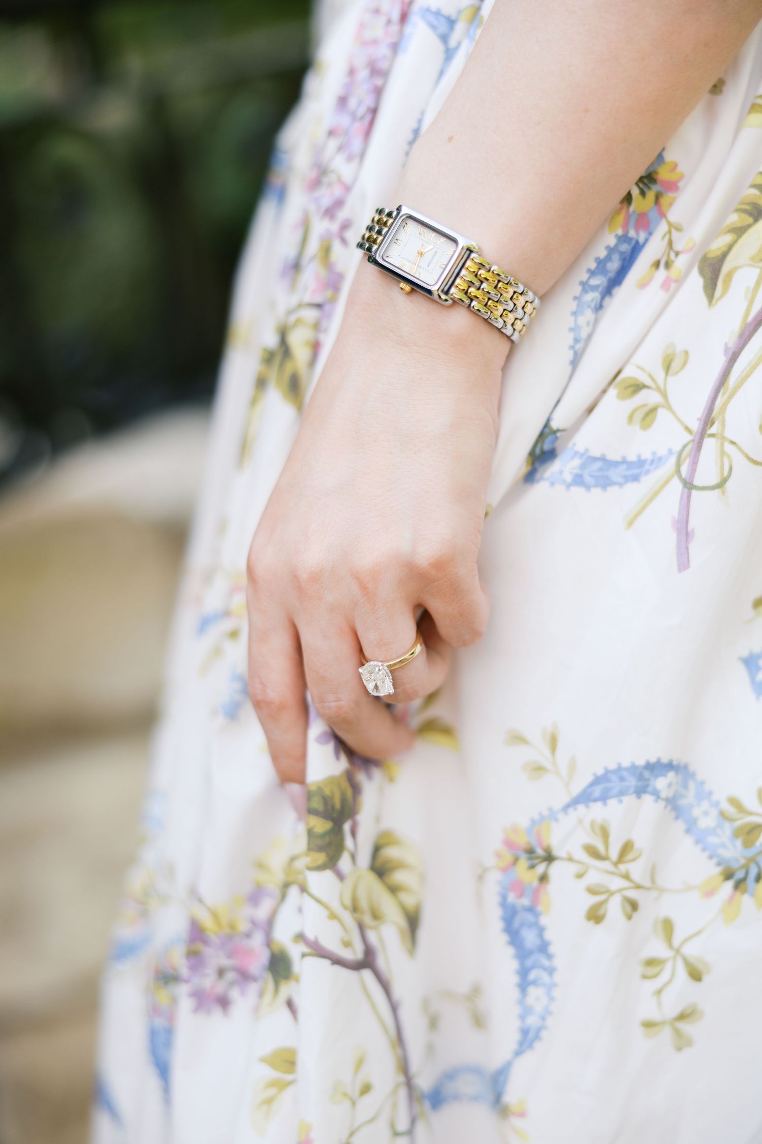 Close-up of a woman's hand wearing a gold diamond ring and two-tone watch, against a floral print dress at Dallas Arboretum