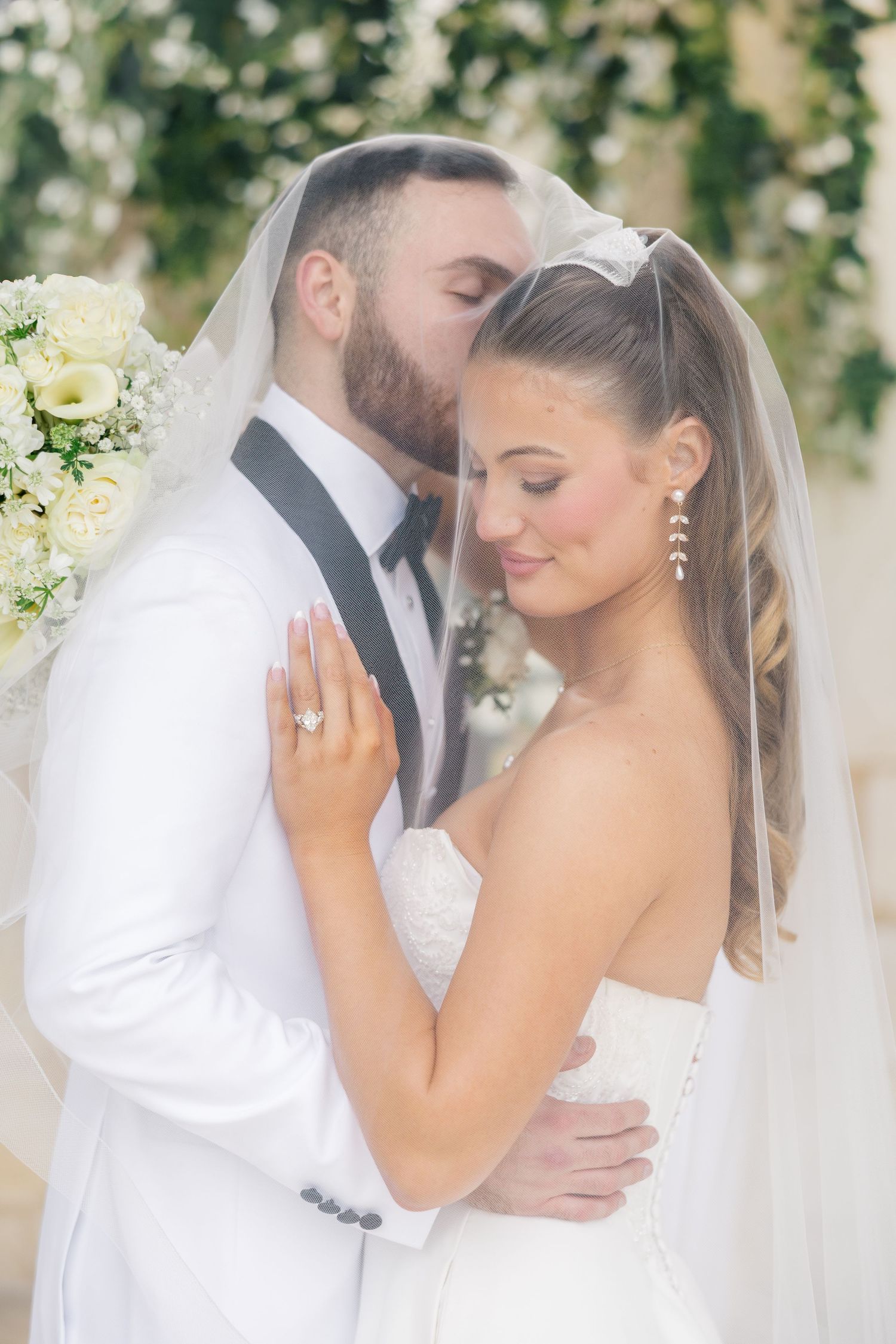 A romantic wedding couple embraces under floral decor in an elegant outdoor setting. The Springs Venue Rockwall TX