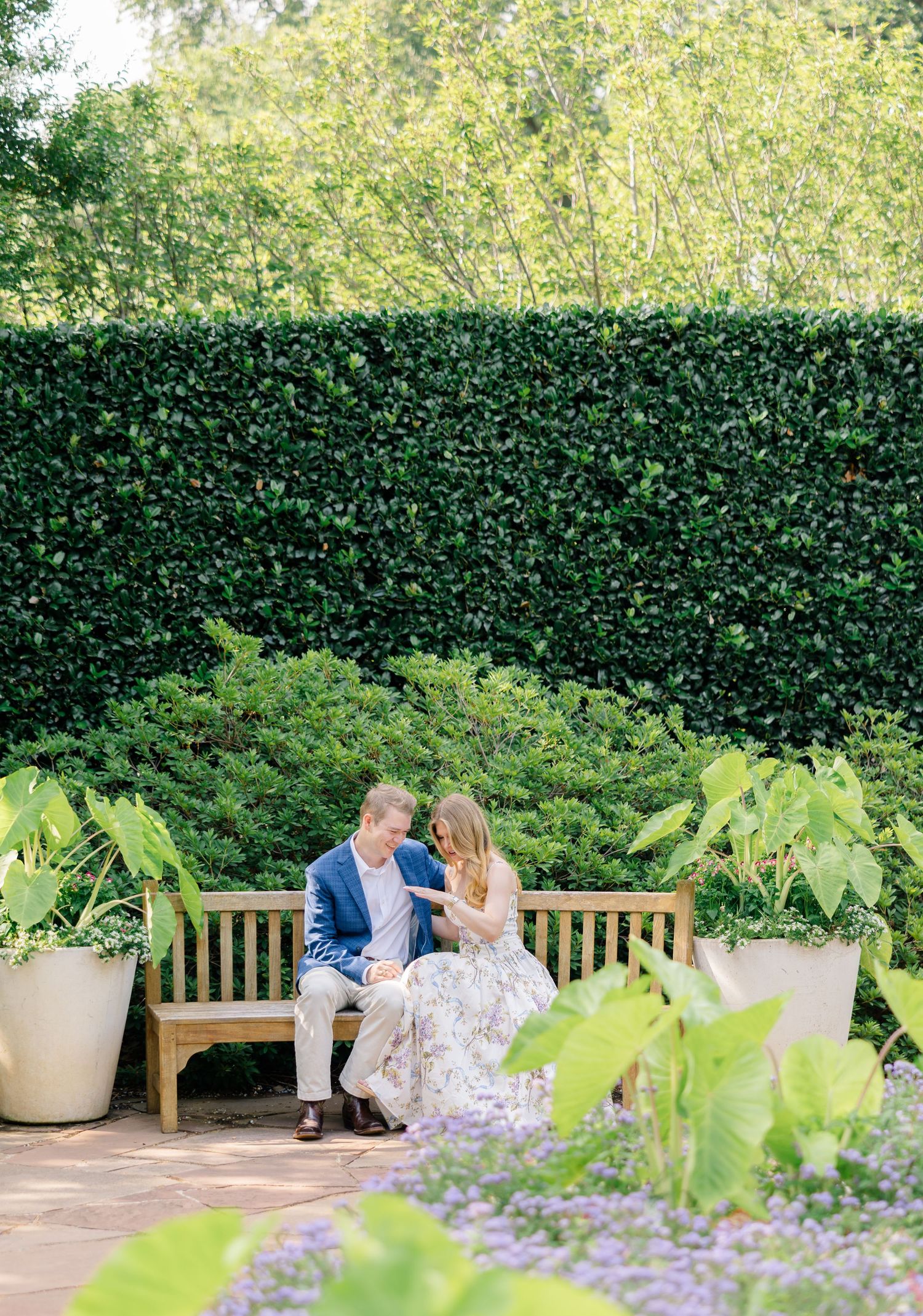Couple sitting on a wooden garden bench surrounded by lush greenery and flowering plants in an elegant outdoor setting at Dallas Arboretum