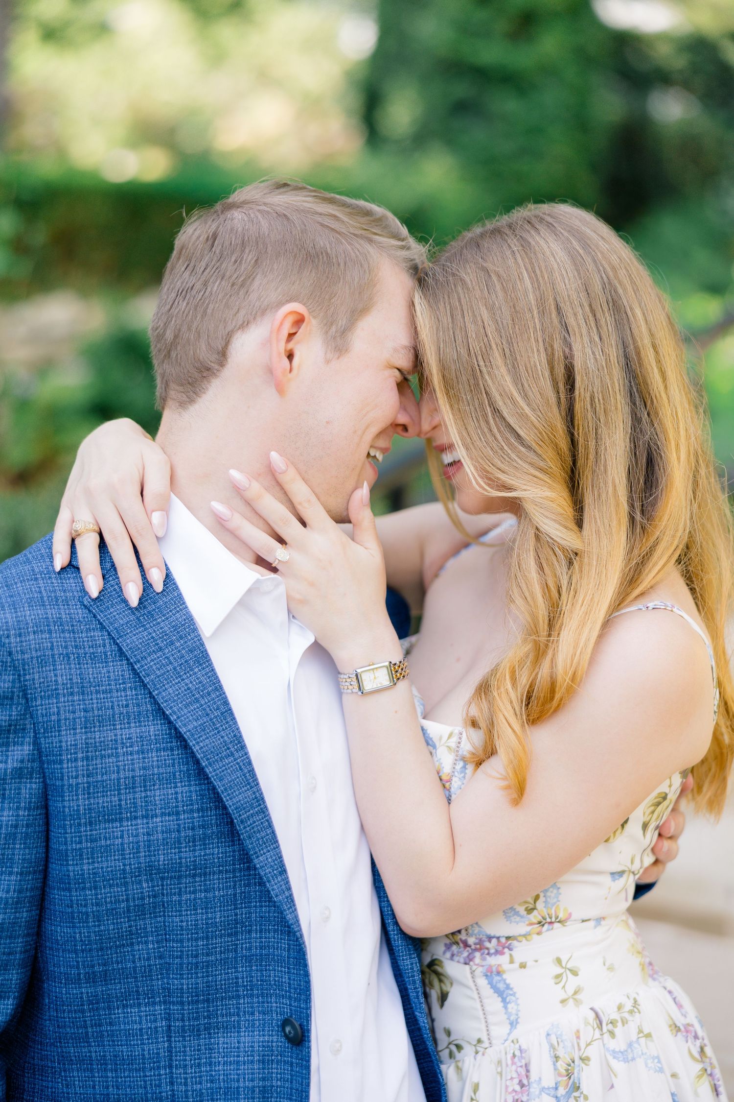 Couple in blue suit and floral dress sharing a romantic forehead touch outdoors, engagement photo at Dallas Arboretum.
