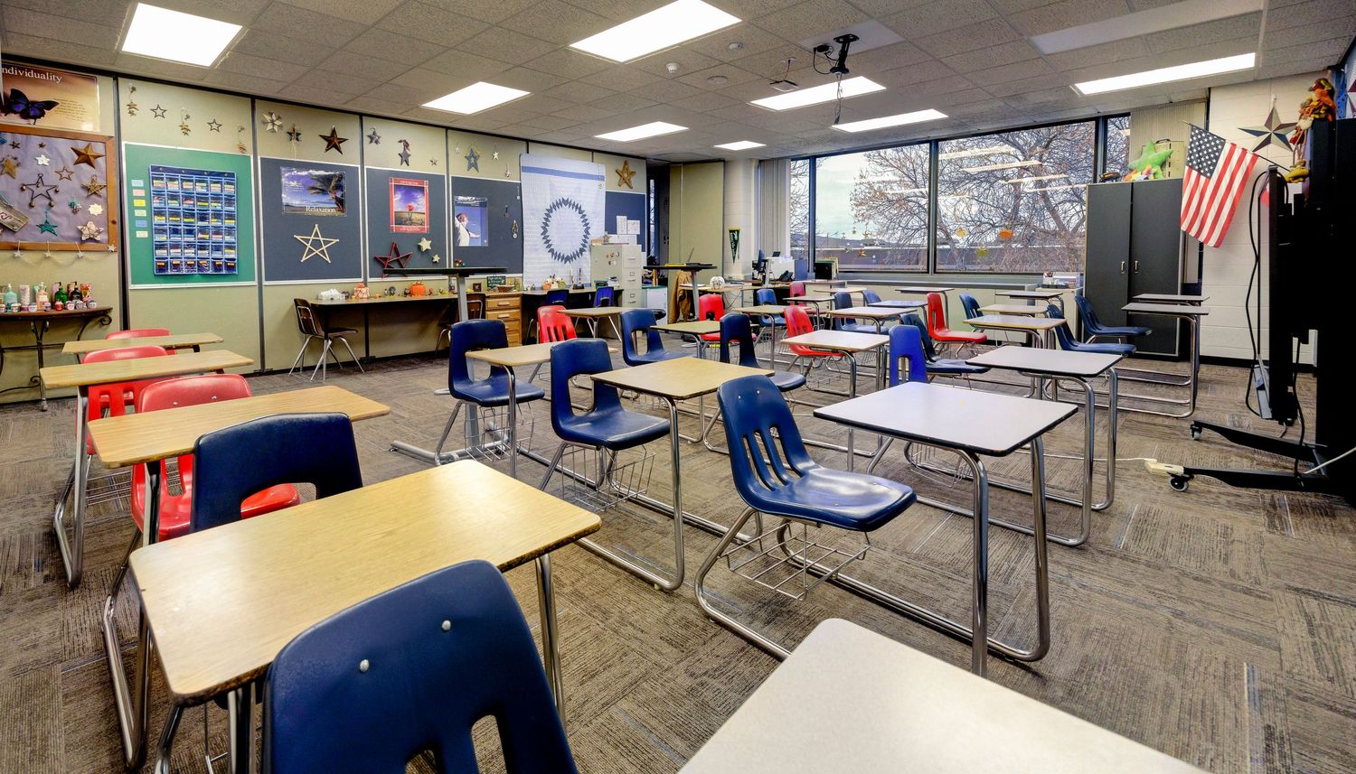 Modern classroom interior with desks, chairs and educational materials displayed on walls.