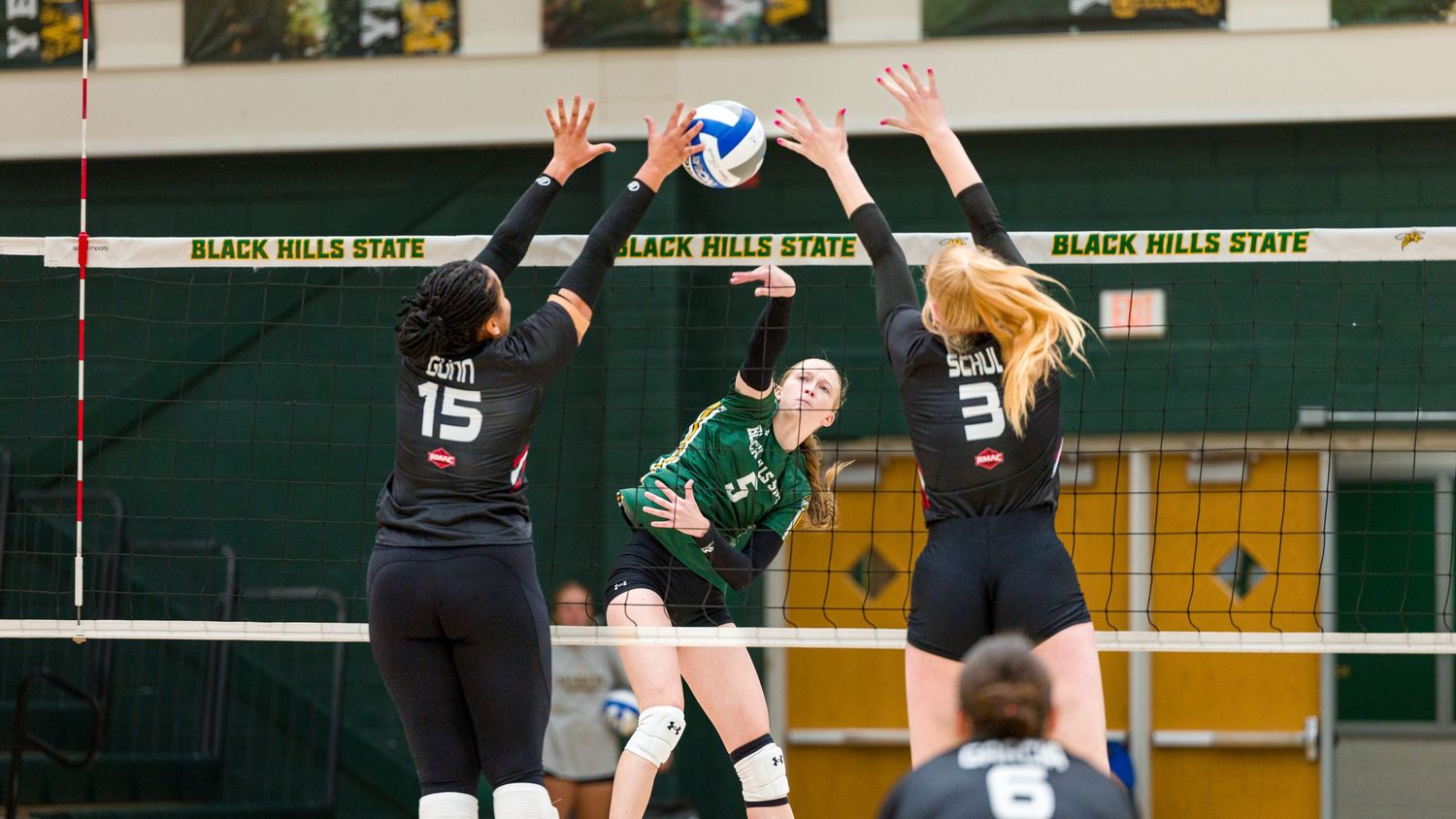 Volleyball players jumping at the net during an indoor match.