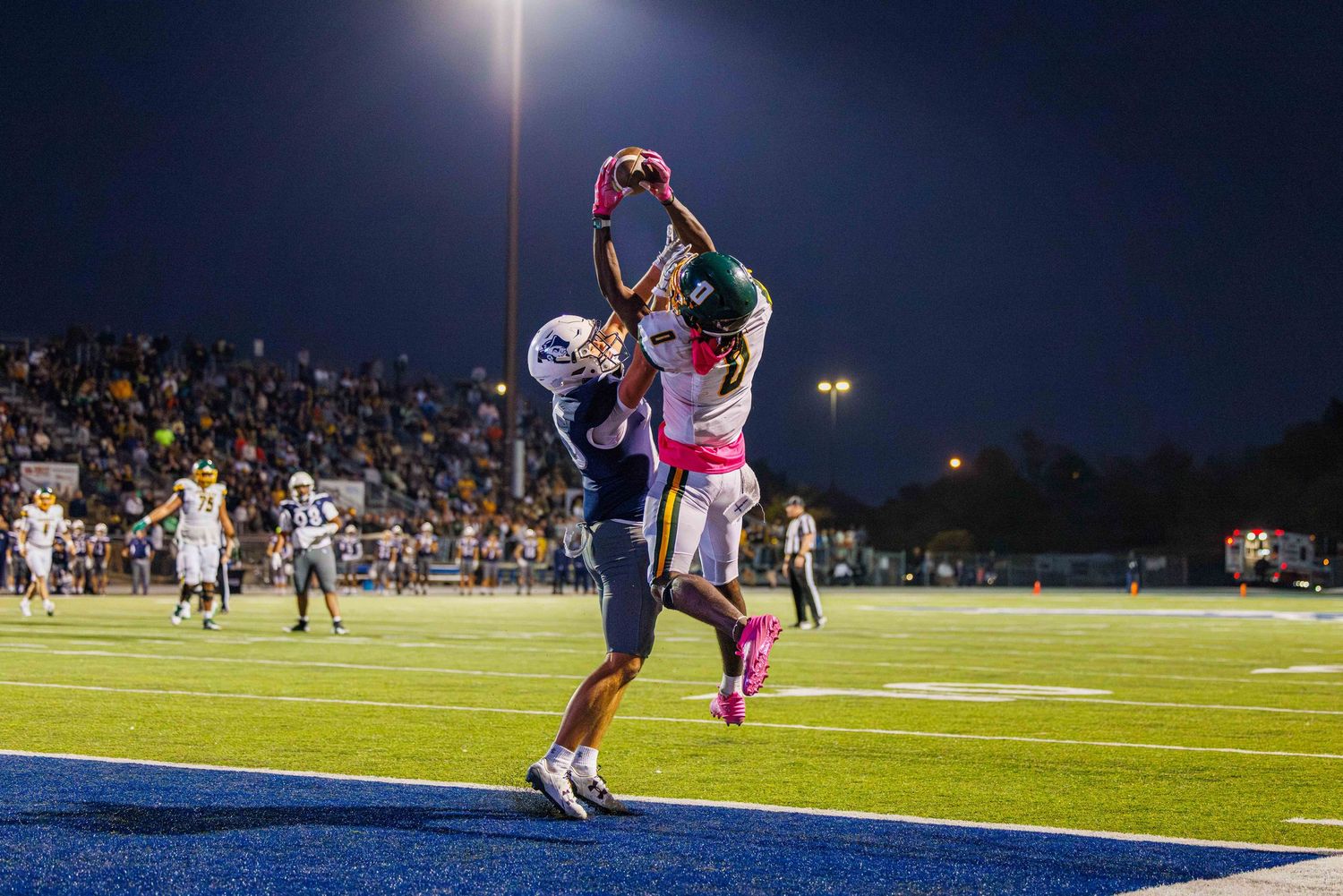 Football player kicks field goal under stadium lights during nighttime game with crowd watching in background.