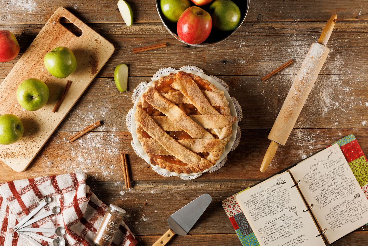 Rustic wooden table with apples, baking ingredients, and recipe pages laid out.