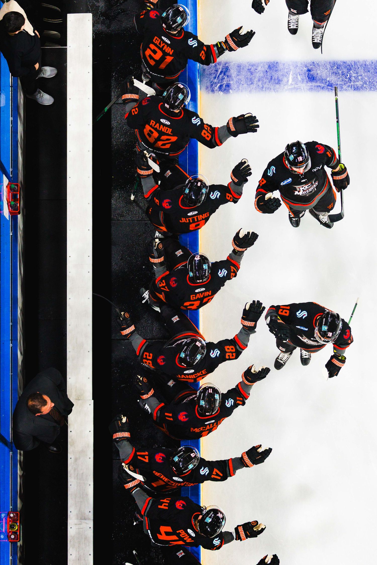 Multiple hockey players in black and orange uniforms celebrate on ice during a game seen from overhead.
