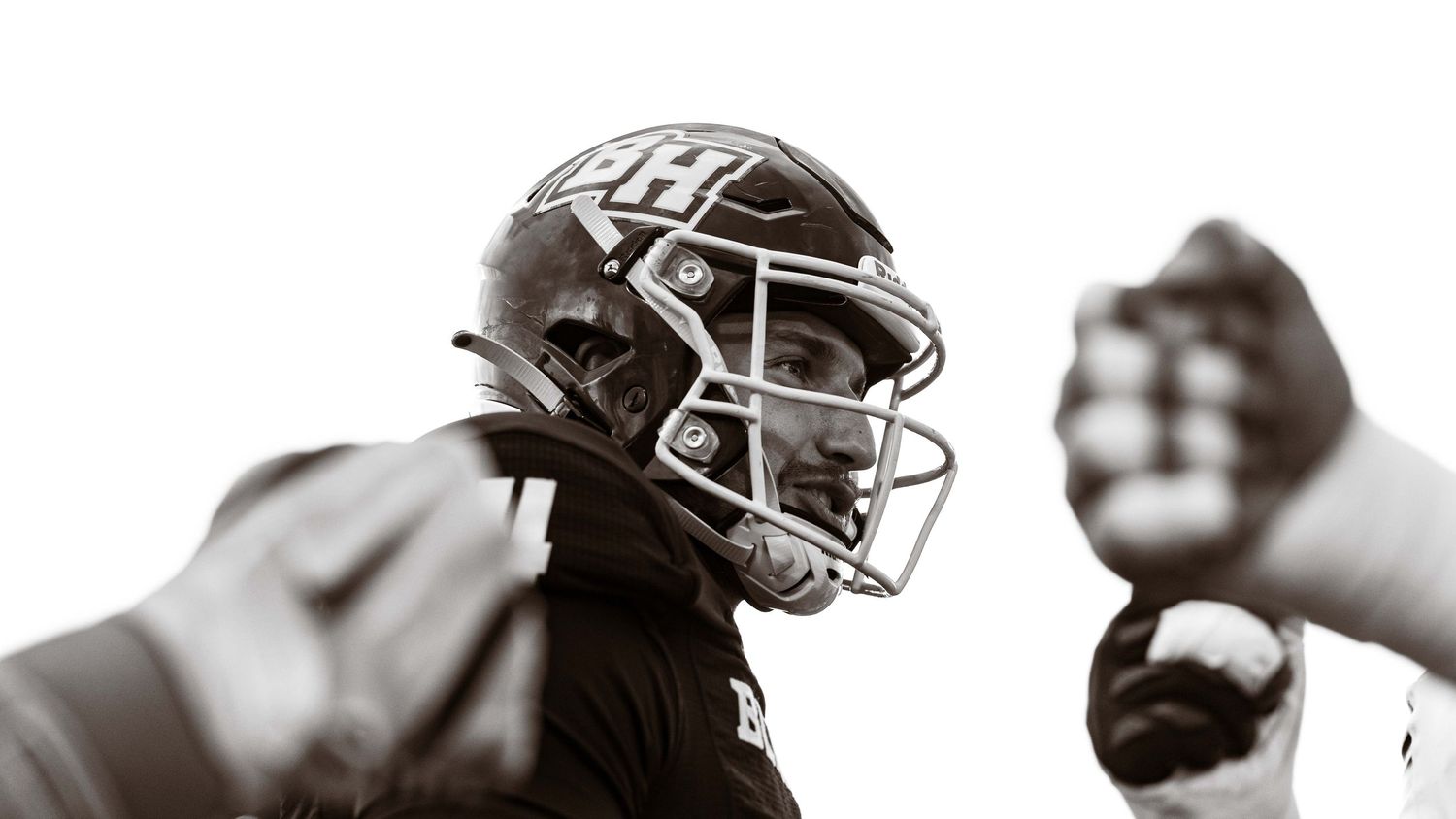 Black and white low angle photo of a football player wearing a helmet looking upward during a game.