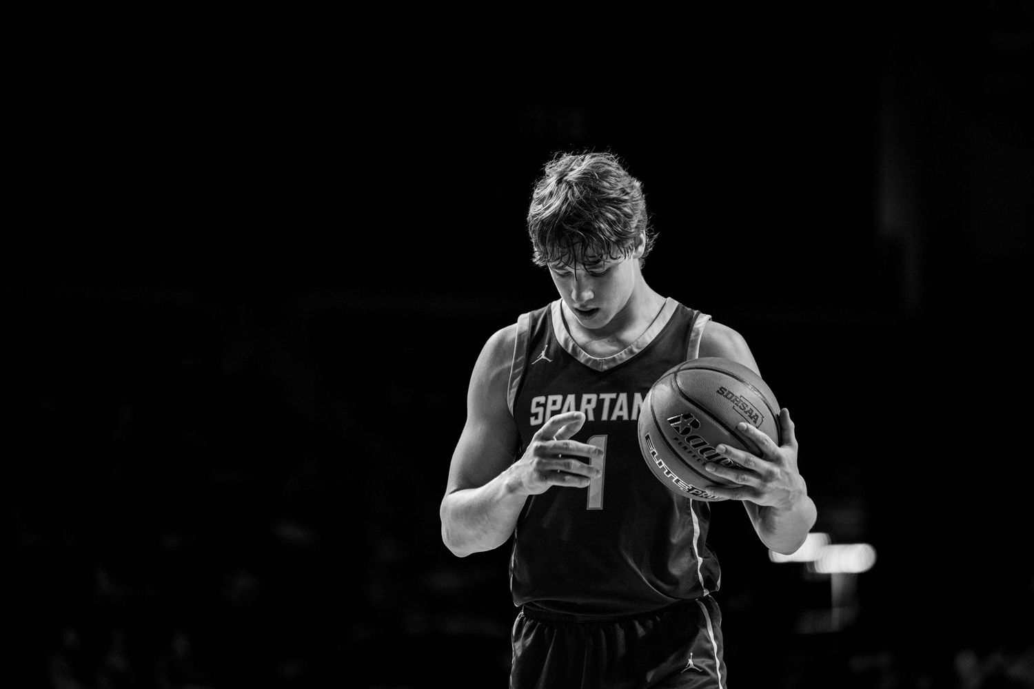 Basketball player in a dark Spartans jersey drives to the basket during an intense game moment.