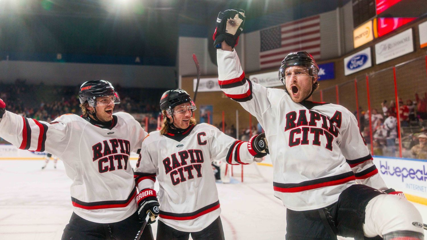 Hockey players celebrate a goal with teammates along the boards during an exciting game moment.