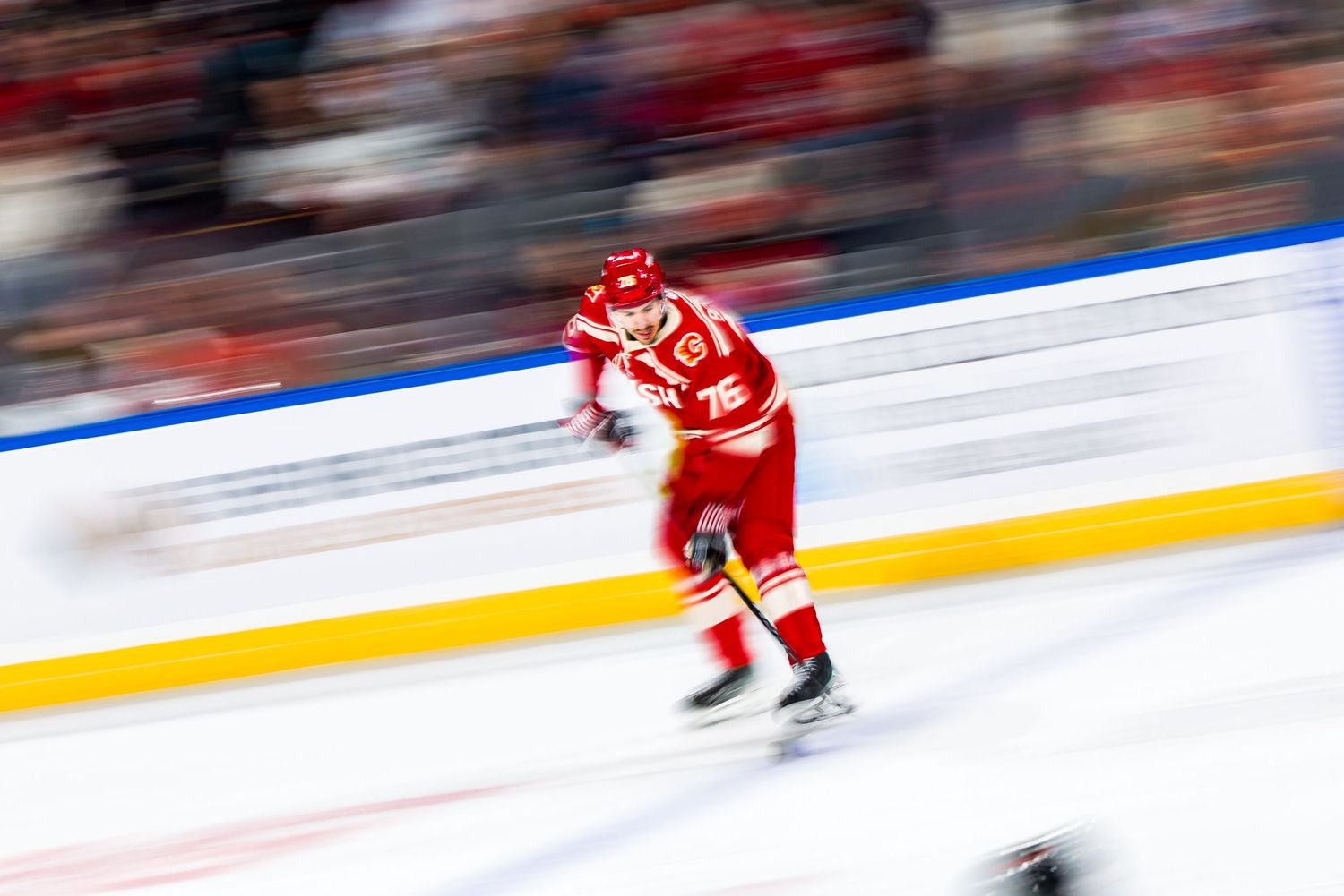 A hockey player in red and white uniform skating at high speed on ice, creating a motion blur effect during gameplay.
