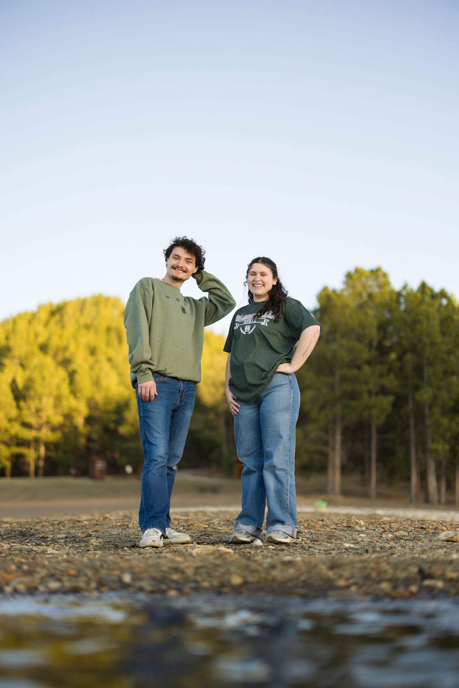 Couple in matching green sweatshirts posing playfully outdoors during golden hour.