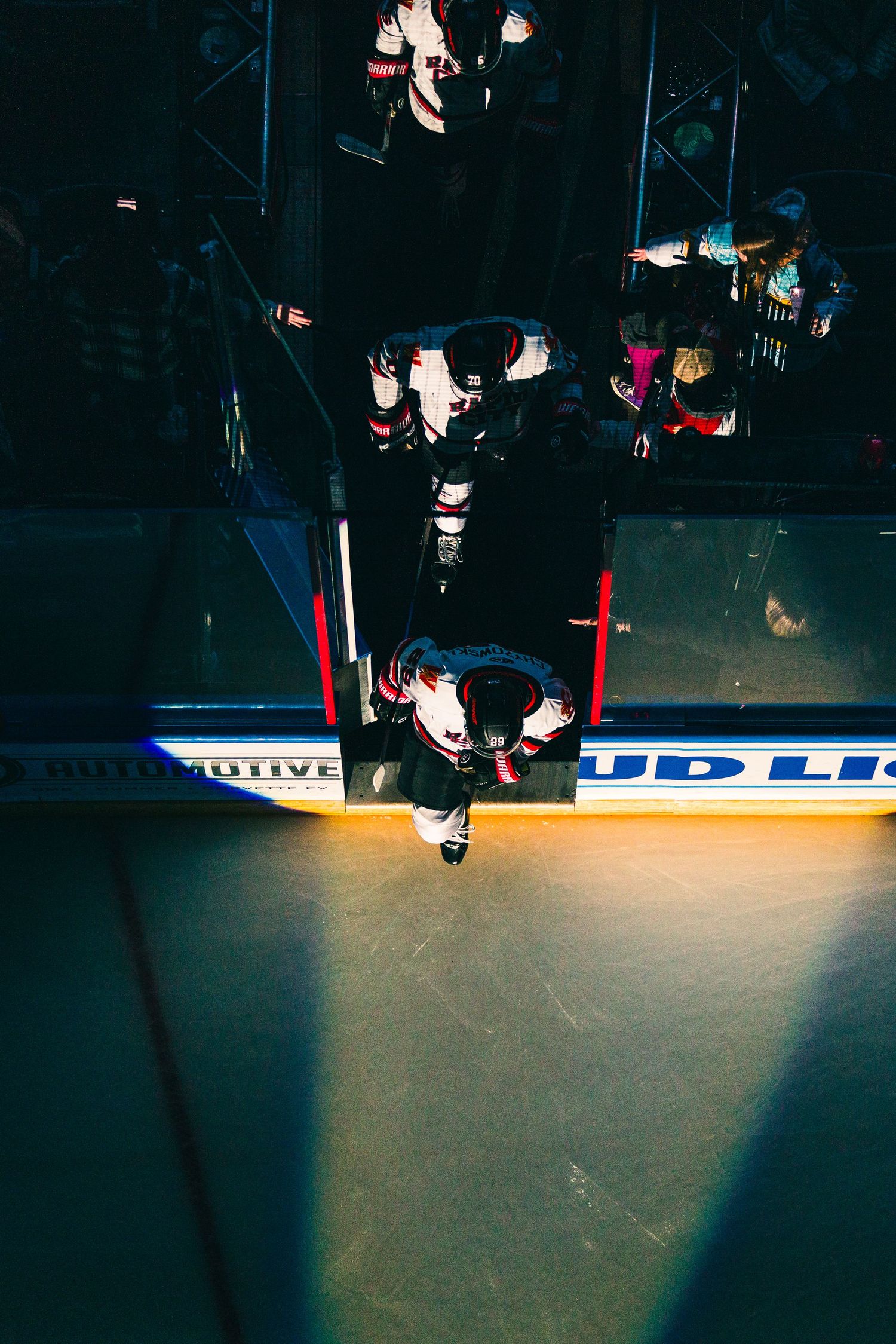 Red goal posts cast dramatic shadows on dark ice rink surface during a hockey game.