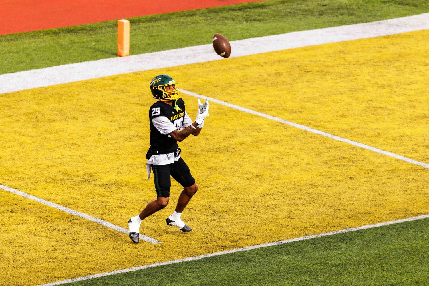 Football player in black and white uniform prepares to catch a pass on a yellow field during practice.