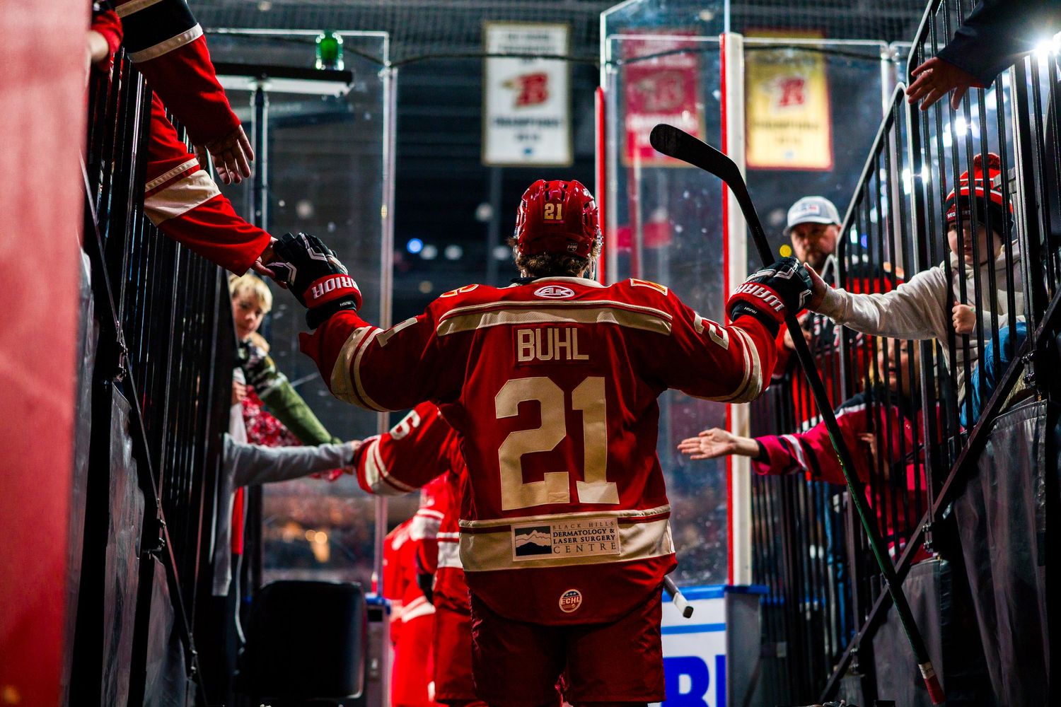 Hockey player in red jersey number 21 celebrates with teammates in the tunnel after a game.