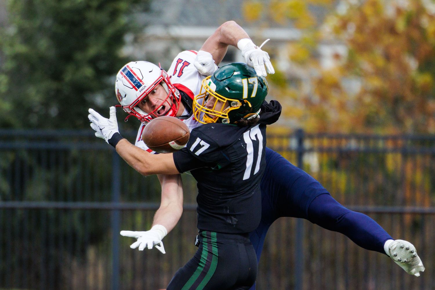 Football players in navy and green uniforms leap to catch a pass during an autumn game.
