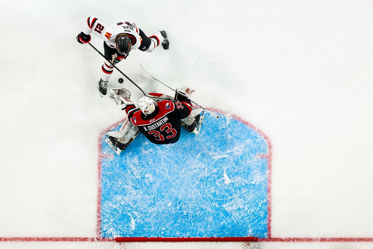 Hockey players battle for control of the puck during an intense game on the blue ice rink.