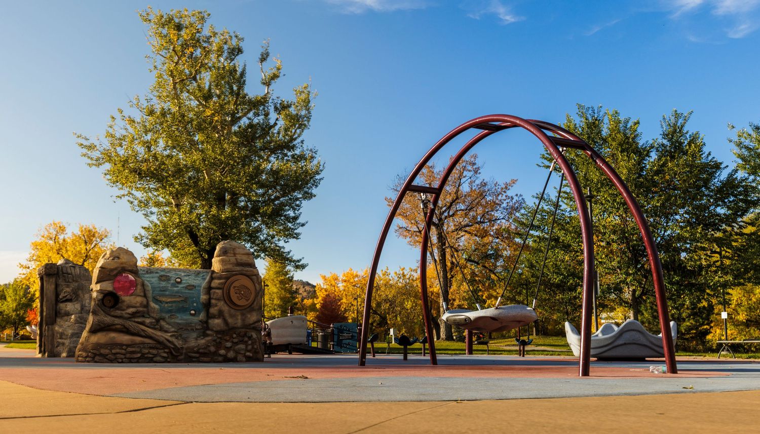 Basketball court with hoops and playground equipment surrounded by autumn trees.