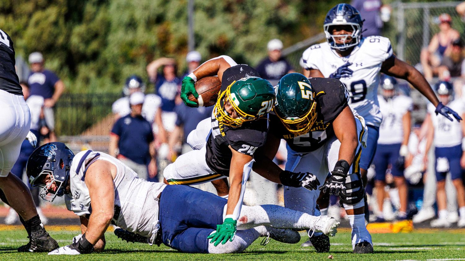 Football players collide during a tackle play with players from both teams diving for the ball.