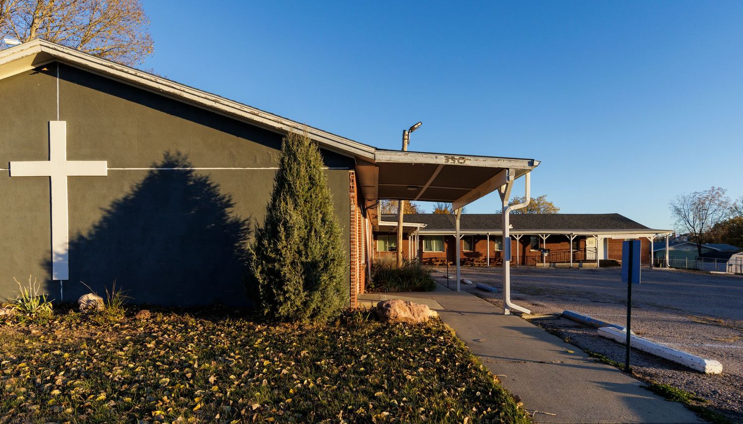 Long exterior view of a single-story church building with white cross against blue sky.