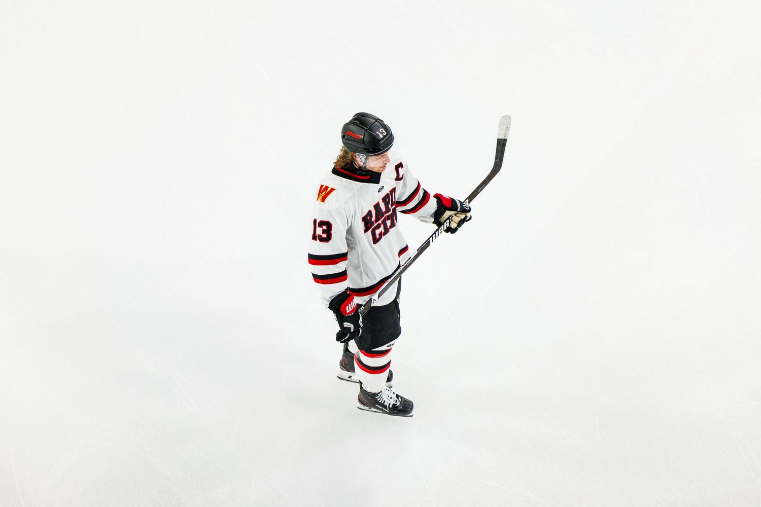 Hockey player in white jersey skates on ice with stick raised during game action.